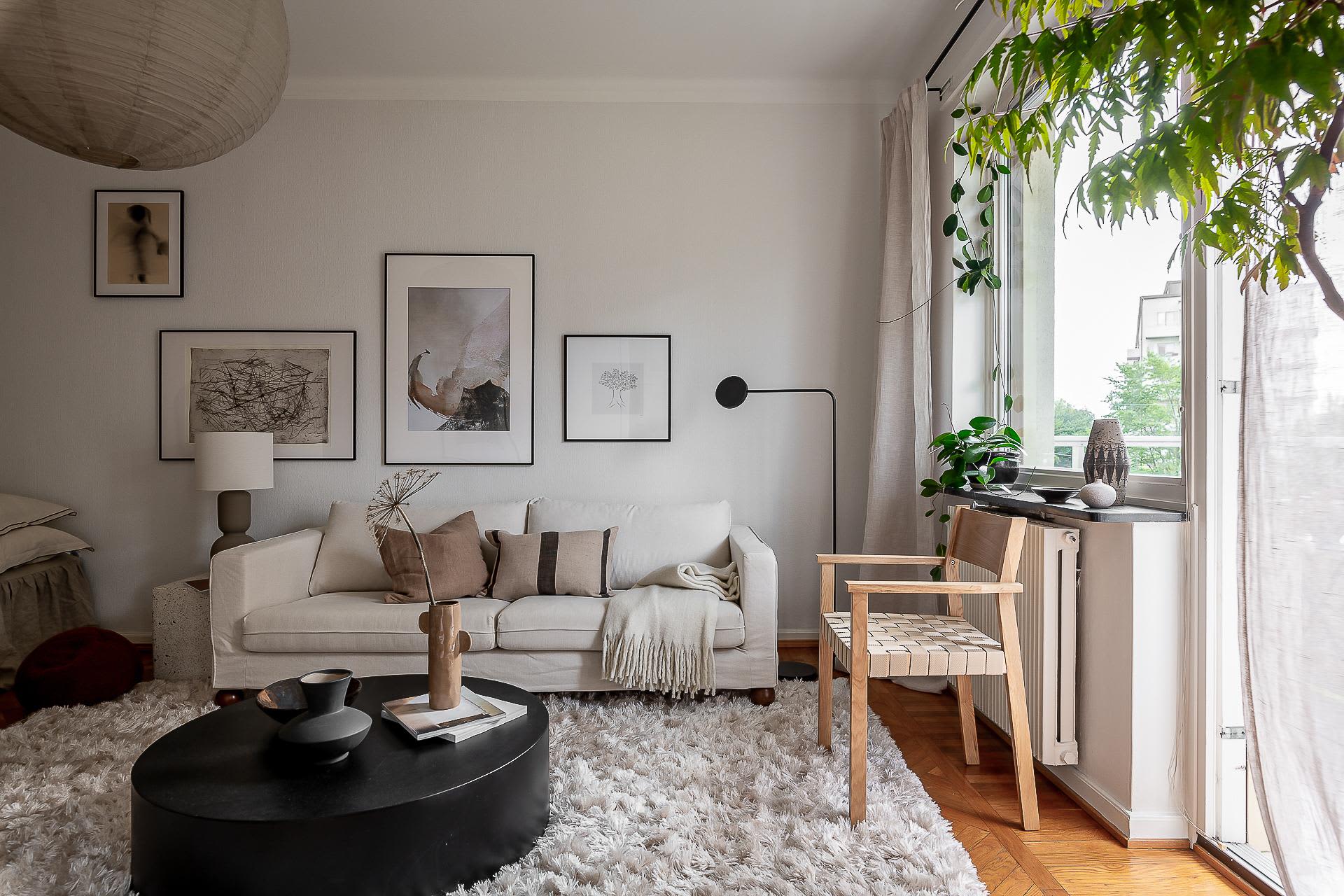 A modern, neutral-toned living room features a cozy sofa, a minimalist coffee table, and a variety of wall art.