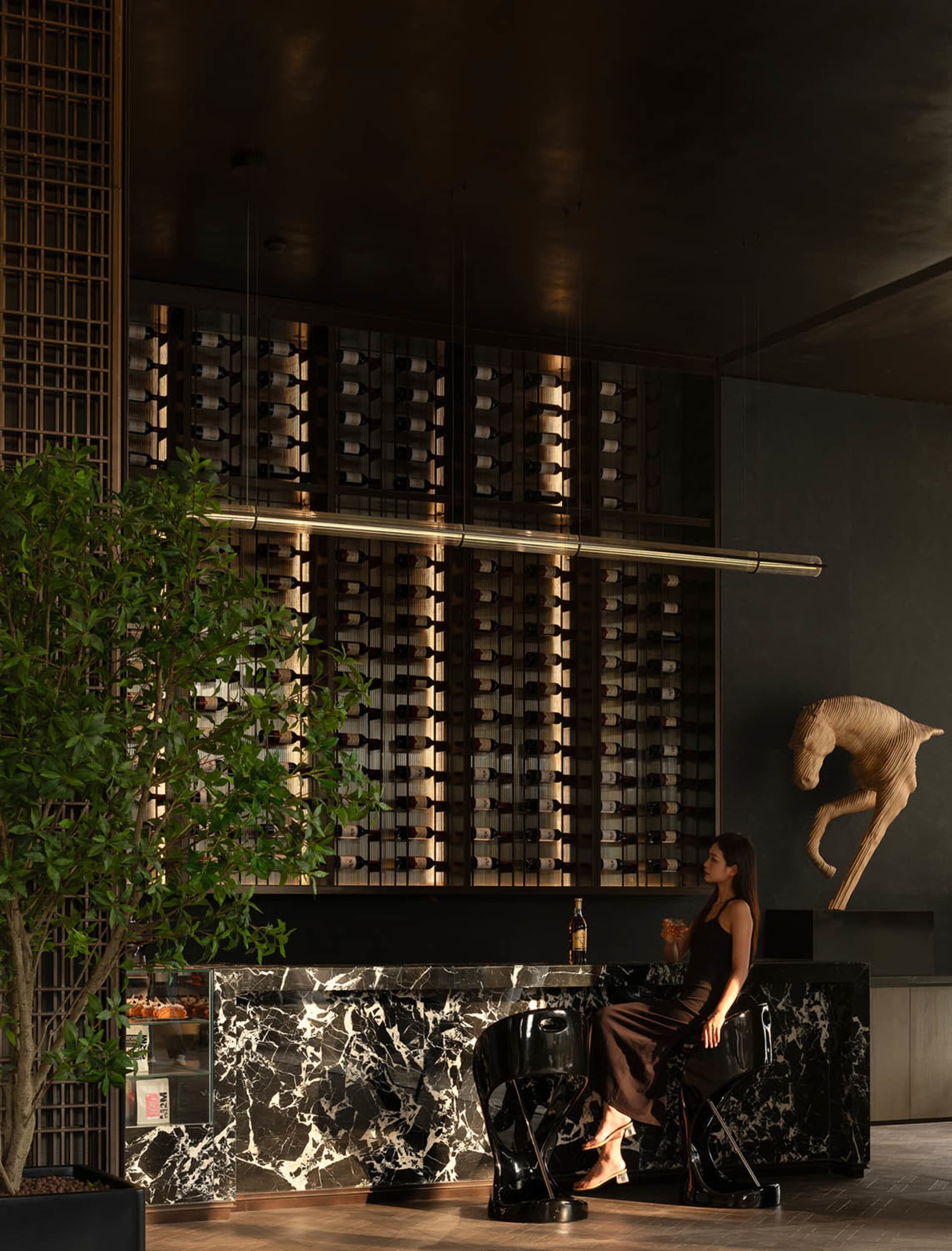 A sleek, contemporary wine bar with a marble exterior and a woman sitting at the bar enjoying a drink.