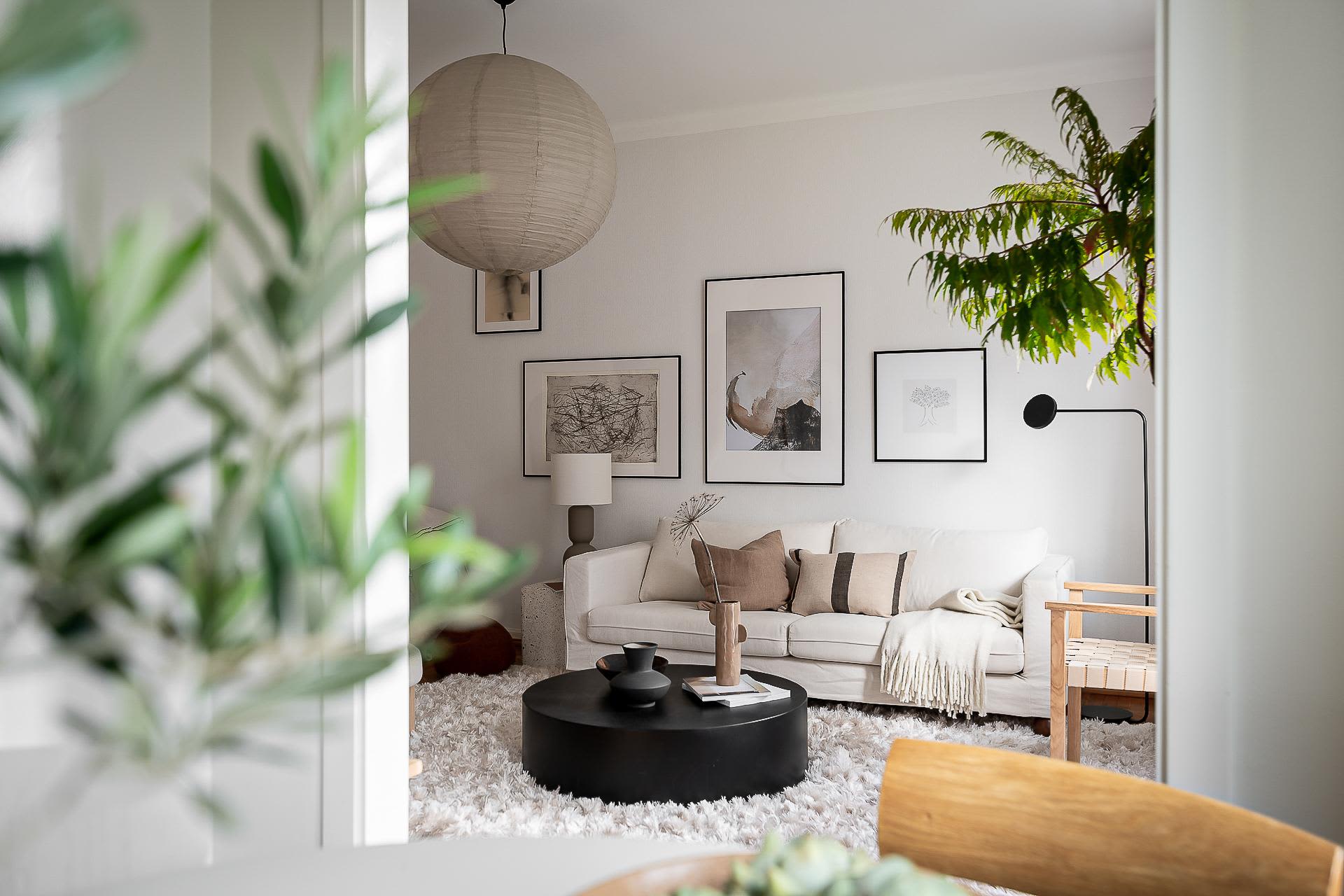 A minimalist living room with a white couch, round black coffee table, and framed artwork on the wall.