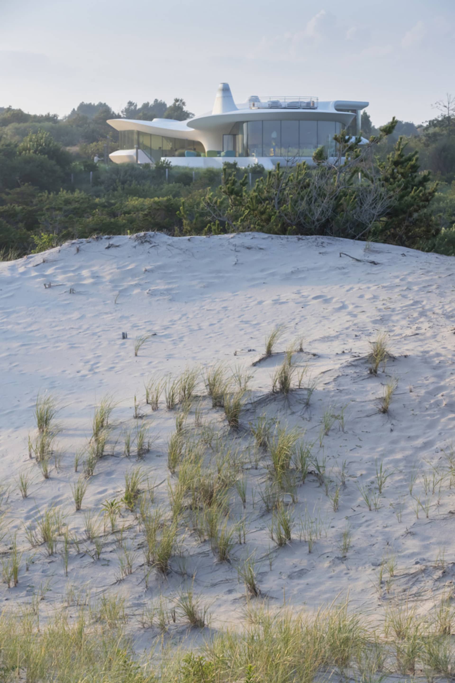 A modern house surrounded by dunes with glass walls and a white, futuristic design.