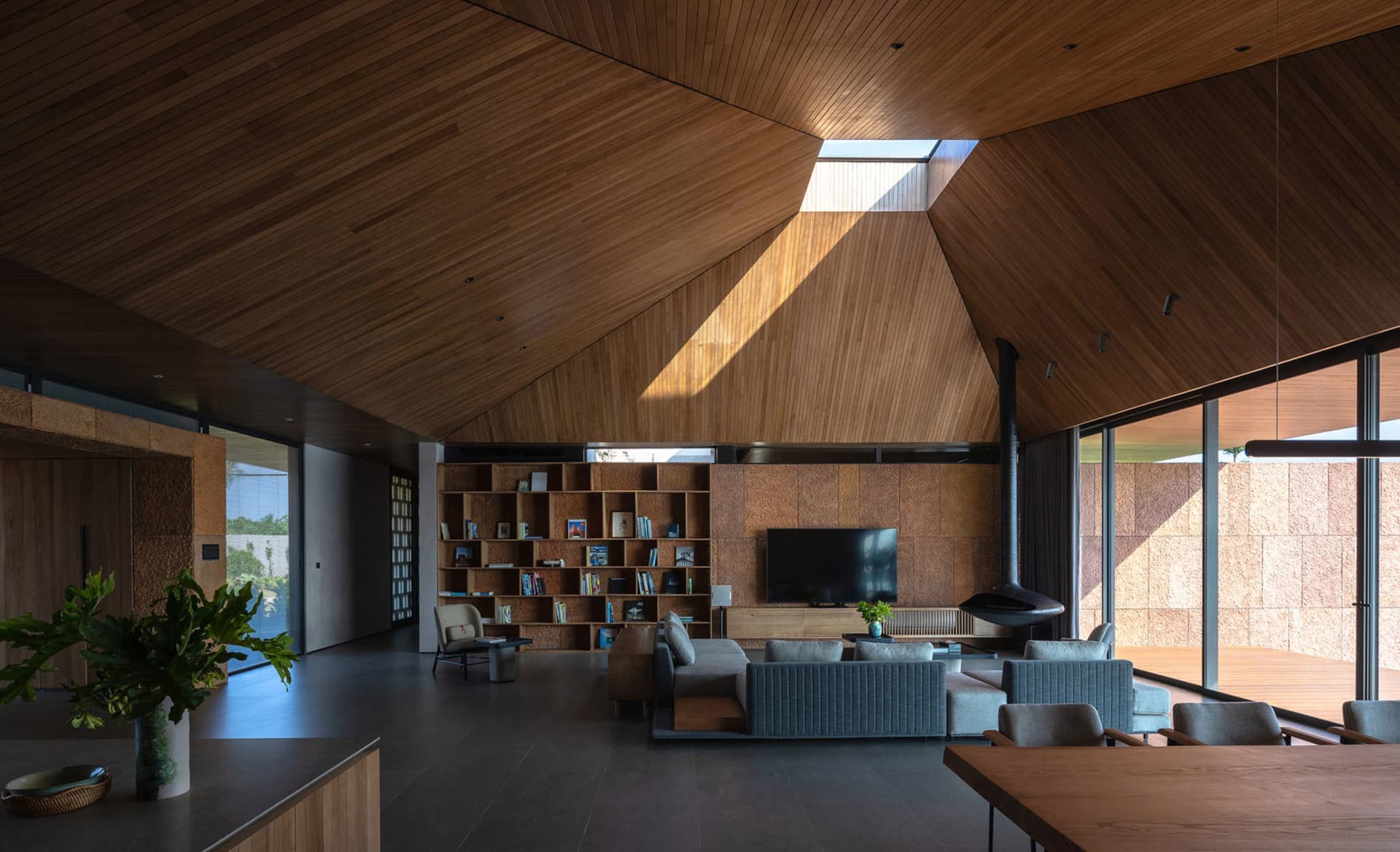 A modern living room featuring wooden walls and floor, with a bookcase, sofa, and TV.