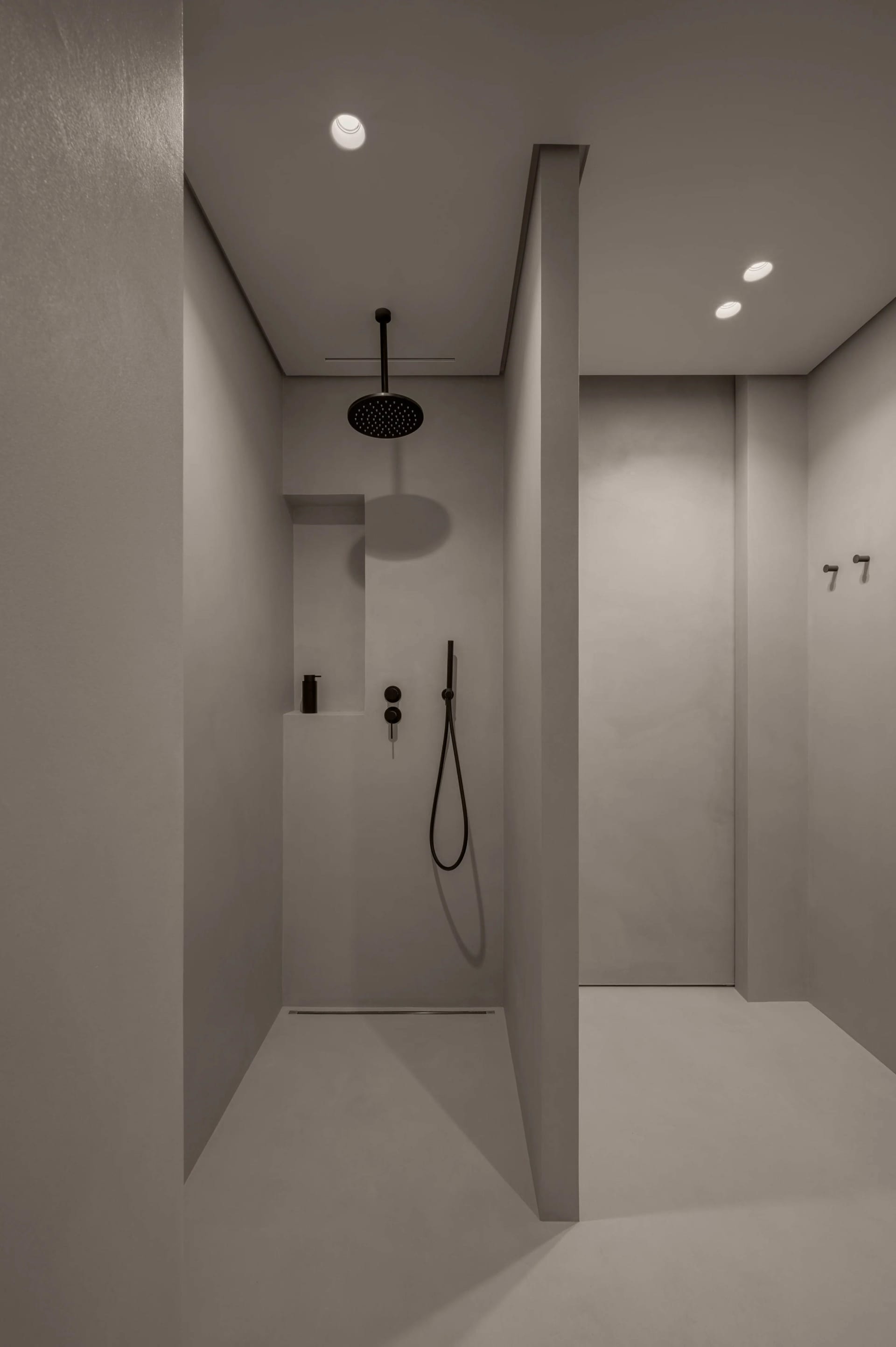 A modern bathroom with concrete walls and ceiling, featuring a black shower head and minimalist design.