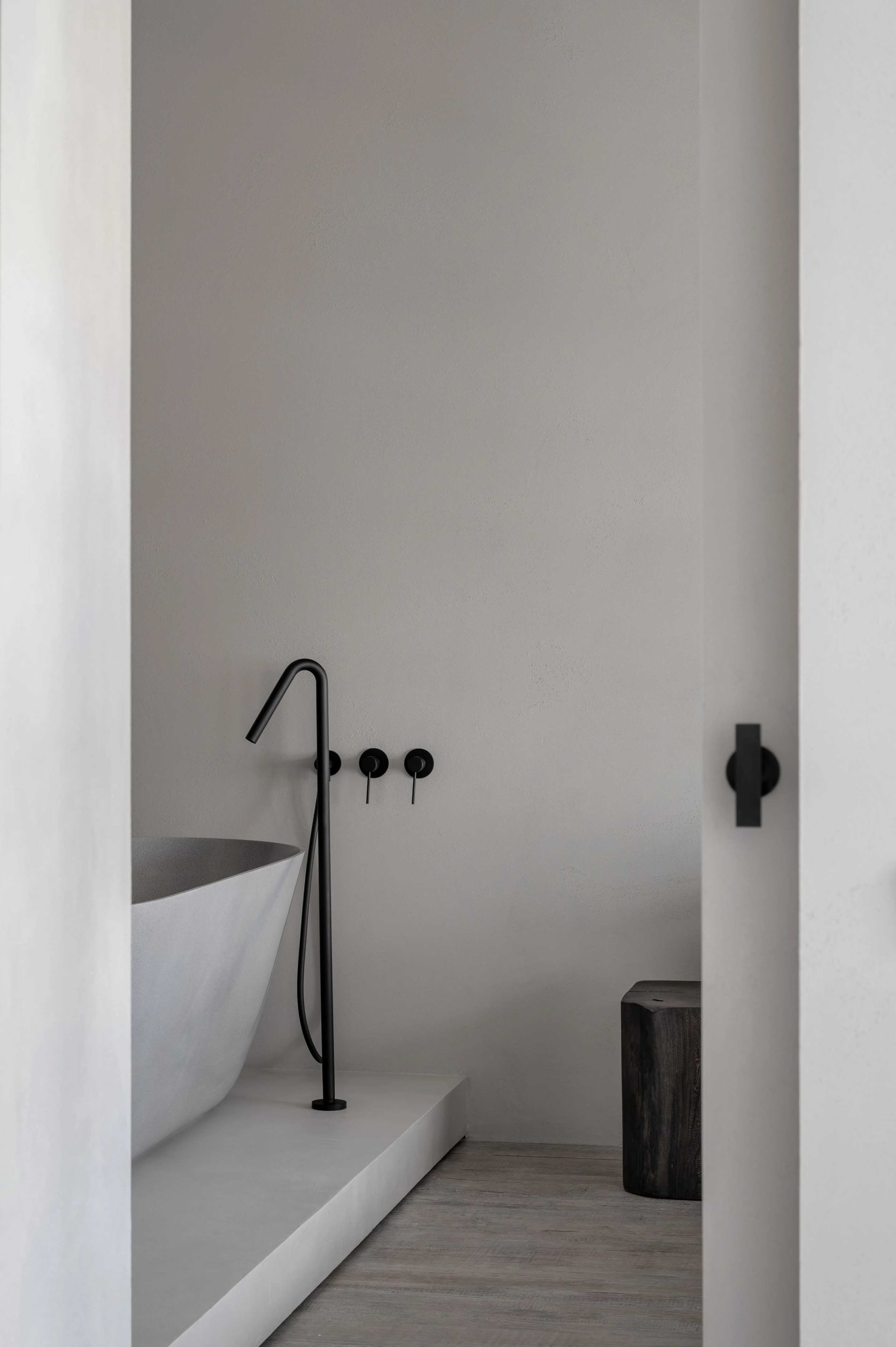 Modern, minimalist bathroom interior featuring a freestanding bathtub made of concrete with black matte hardware.