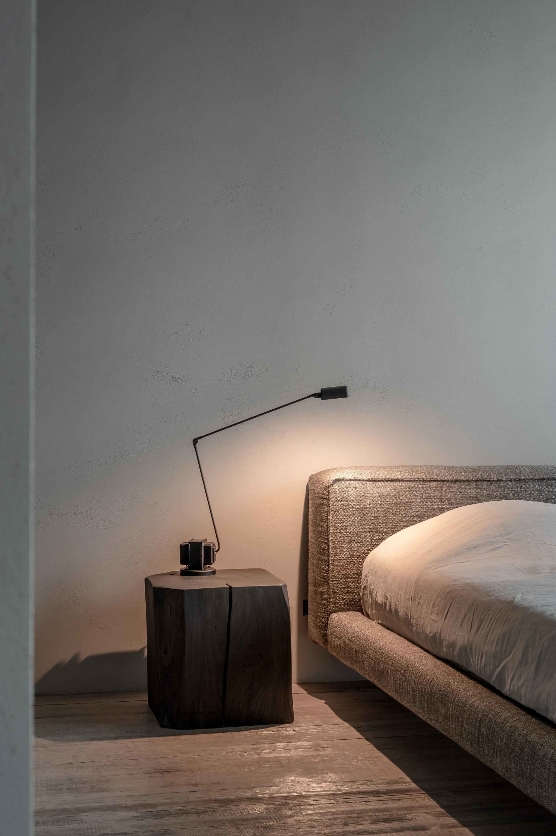 A modern bedroom featuring a textured upholstered headboard and a wooden bedside table with a sleek lamp.