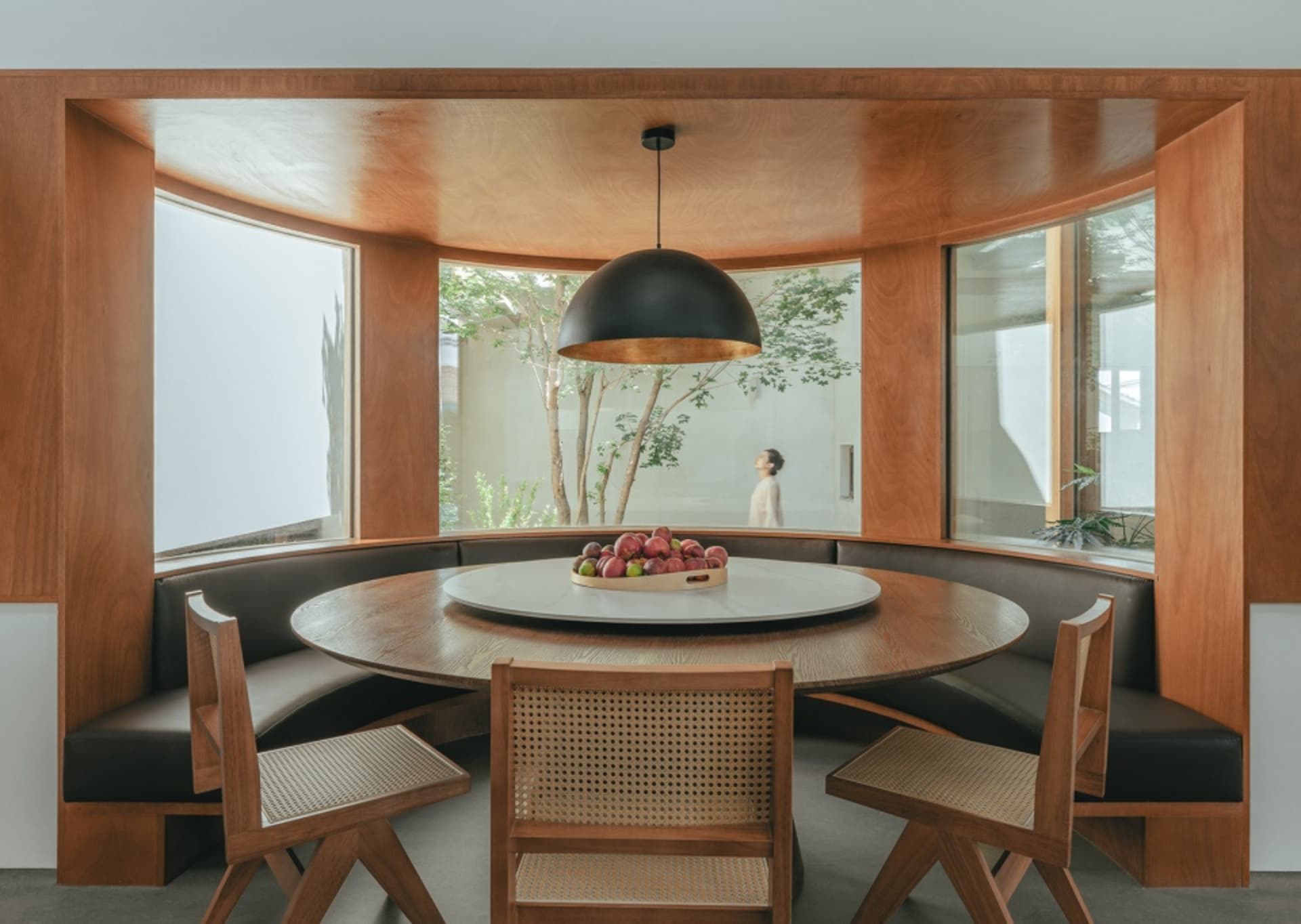 Modern dining area with round table, seating banquette, and black pendant light.