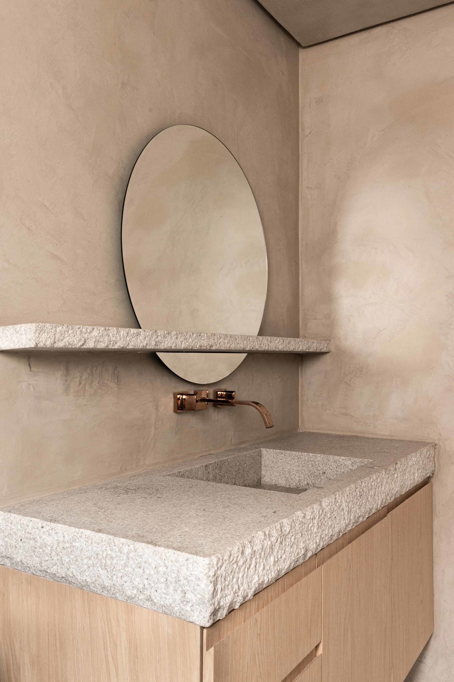 A minimalist bathroom featuring a granite countertop sink and a round mirror on the wall.
