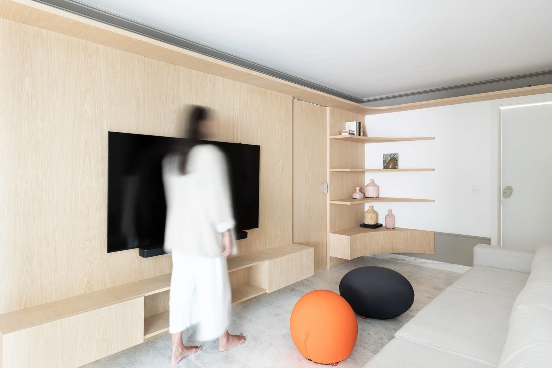 A modern living room featuring a flat-screen TV mounted on the wall, wooden paneling, and plush seating areas with orange and