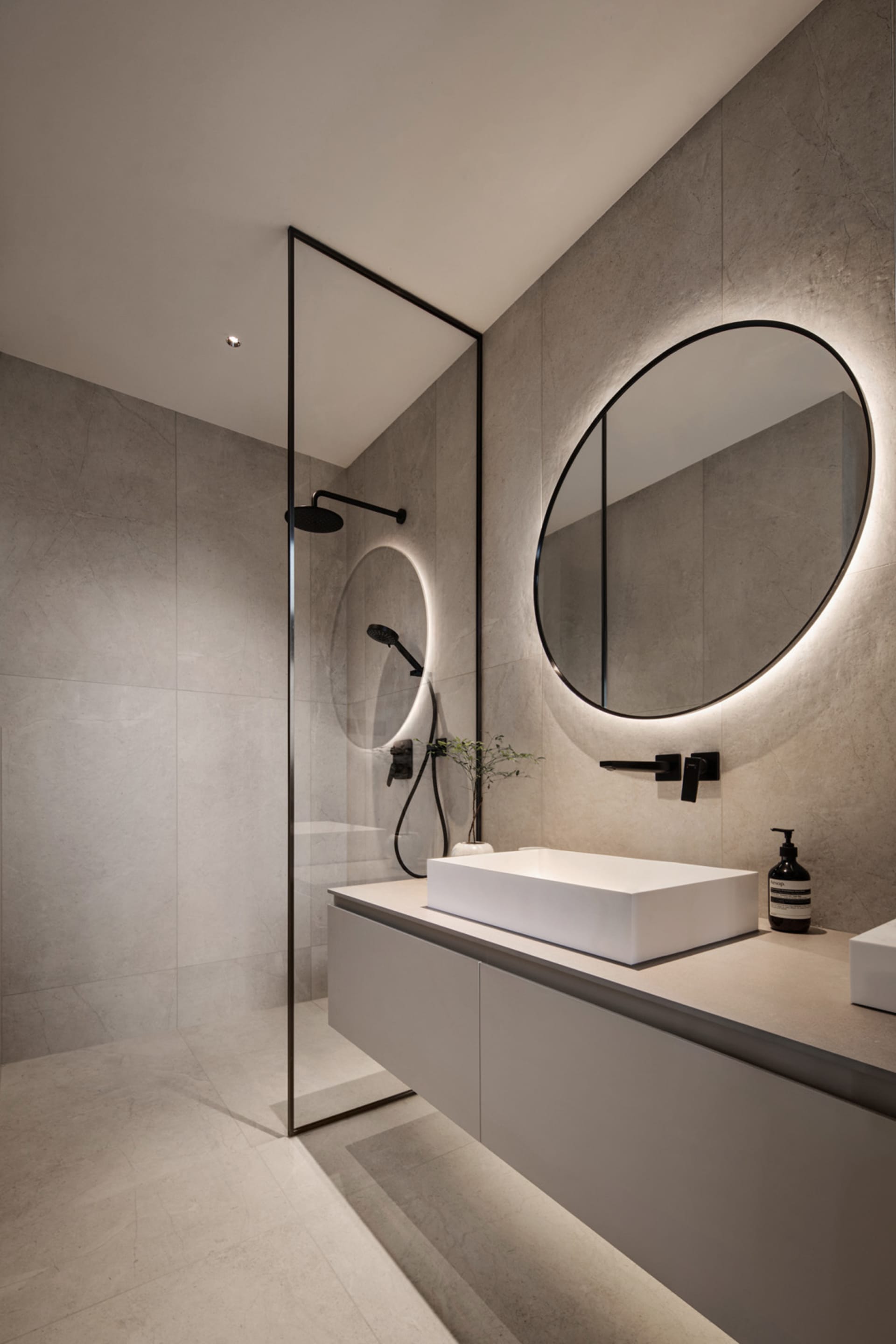 A modern bathroom featuring a minimalist design with concrete walls and floor, a white rectangular sink, and circular mirror