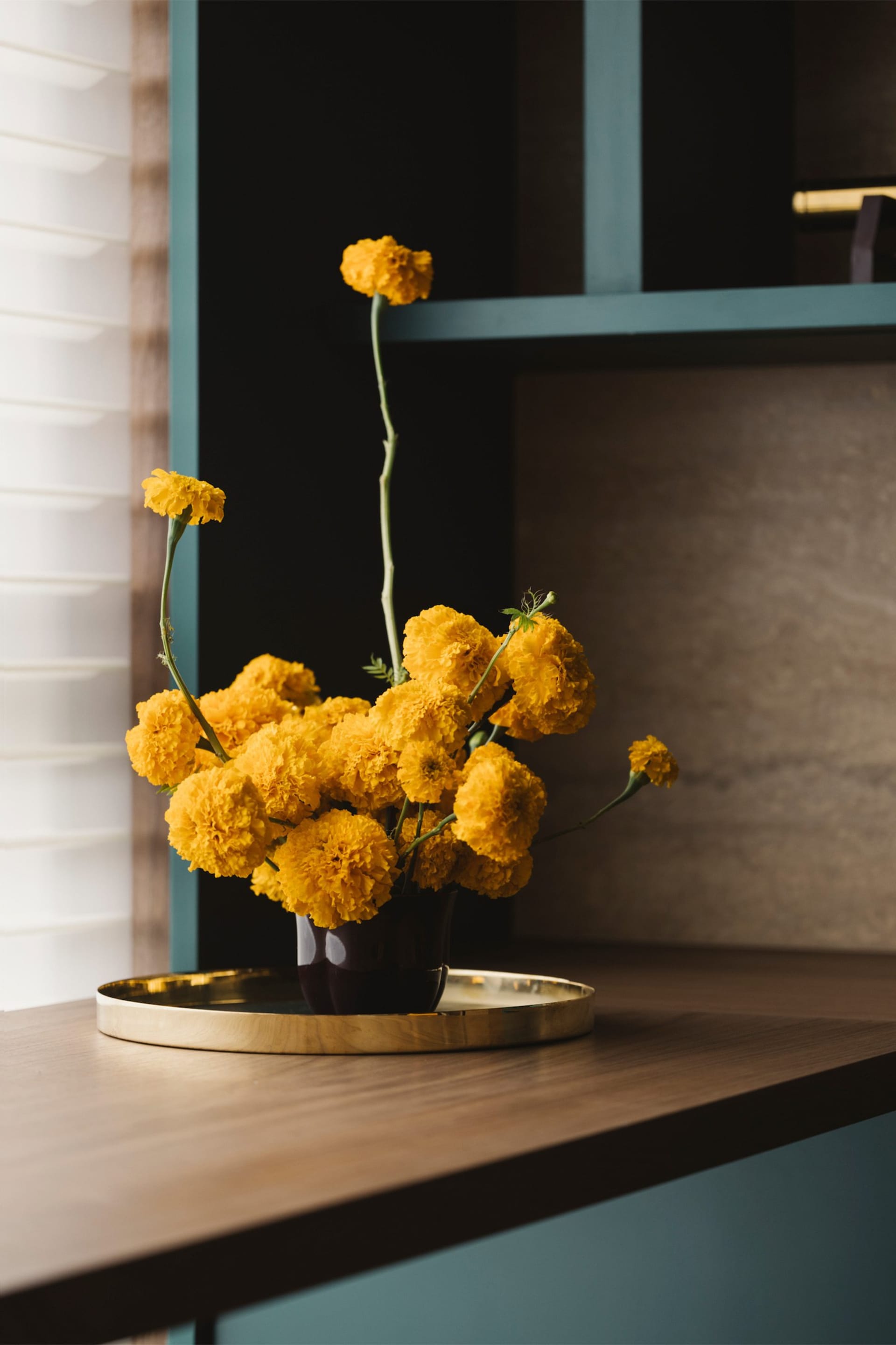 A modern floral arrangement in a metallic vase on a tray, placed on a wooden surface.