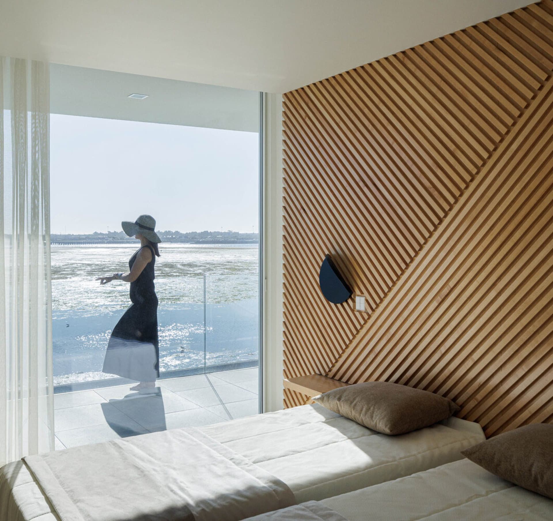 A modern bedroom featuring a bed with a wooden headboard and an ocean view.