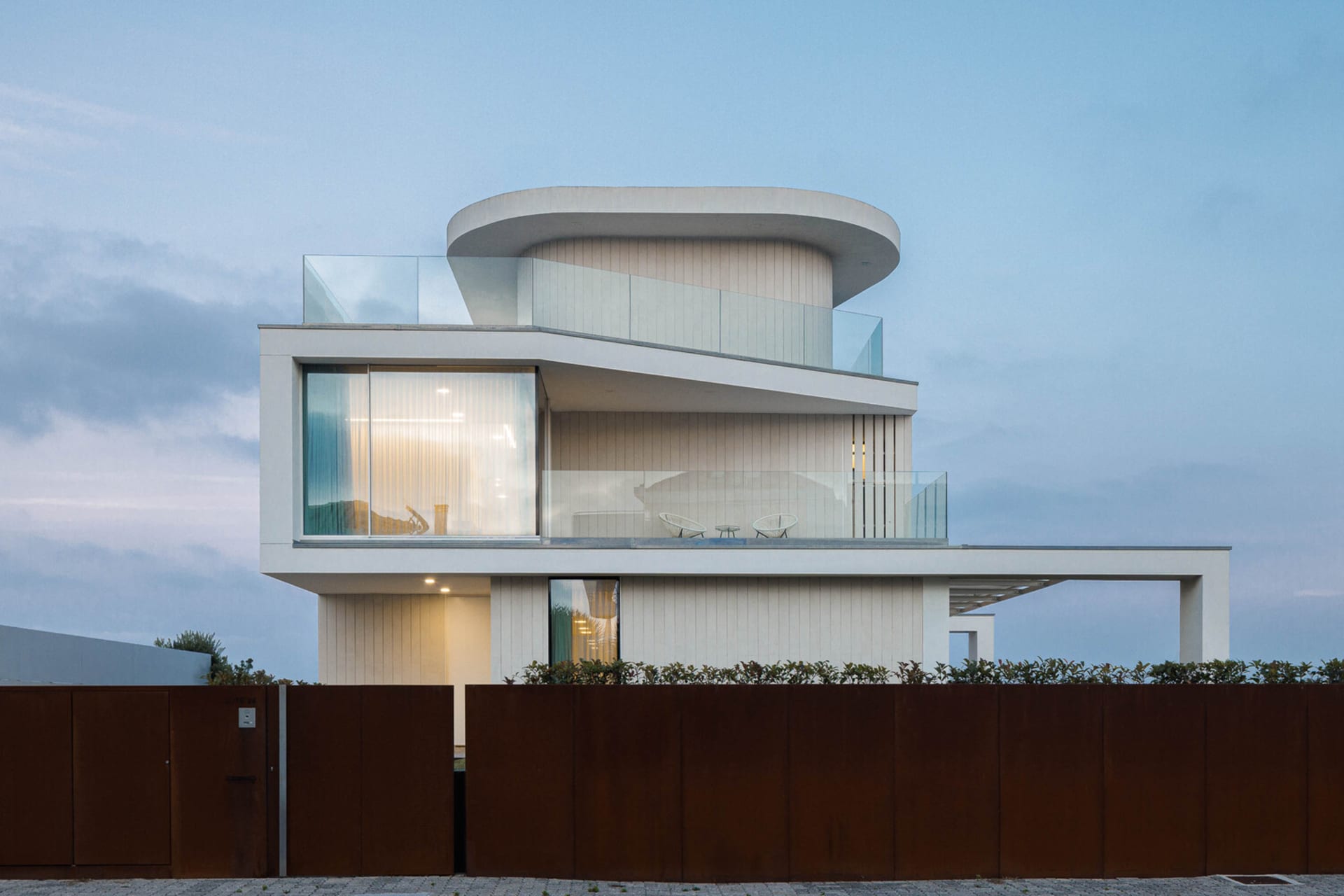 Modern residential house with metal cladding and wood panels, featuring large glass windows and a curved roof.