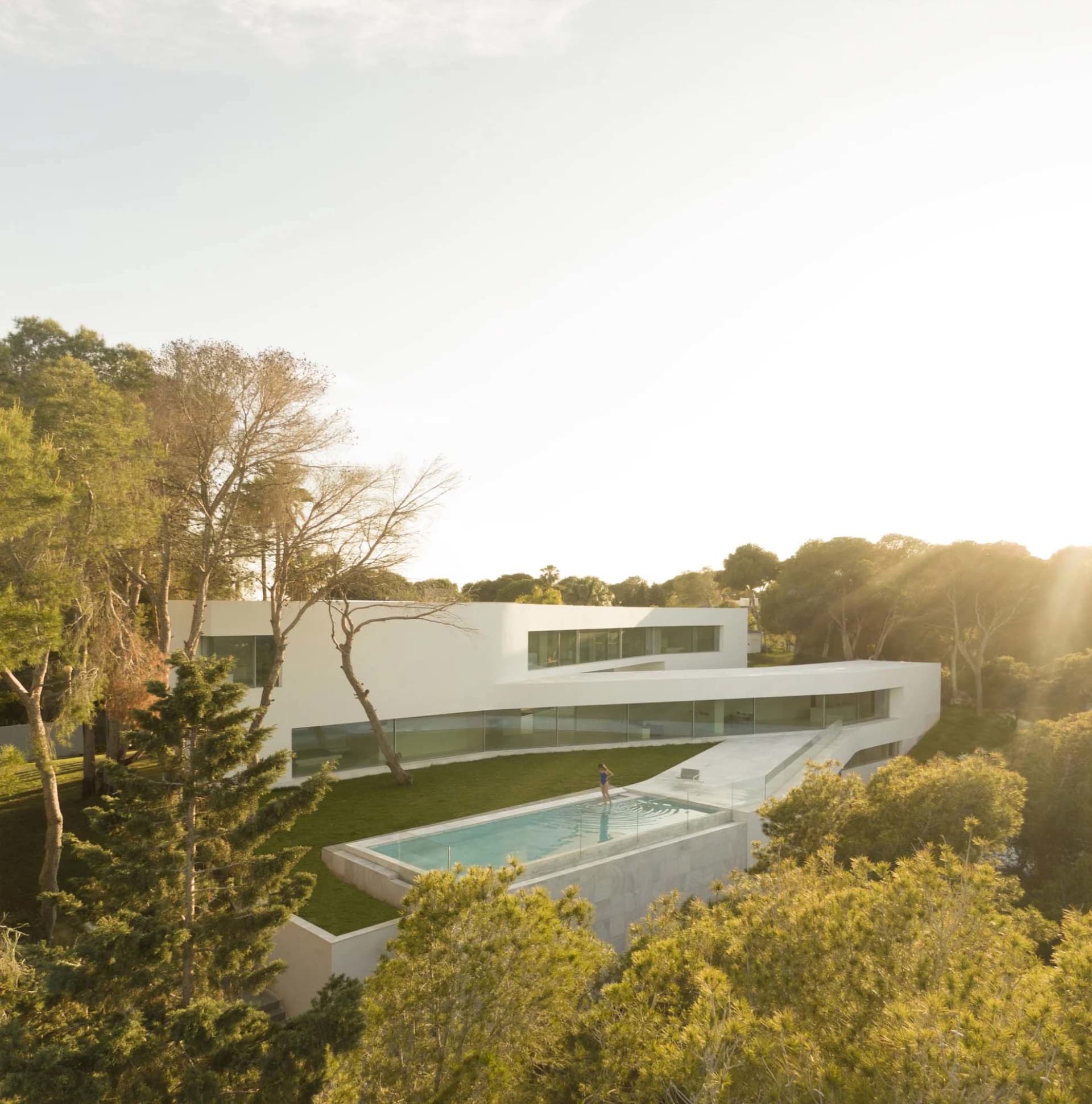 Modern house with swimming pool surrounded by trees, featuring large glass windows and white stone.