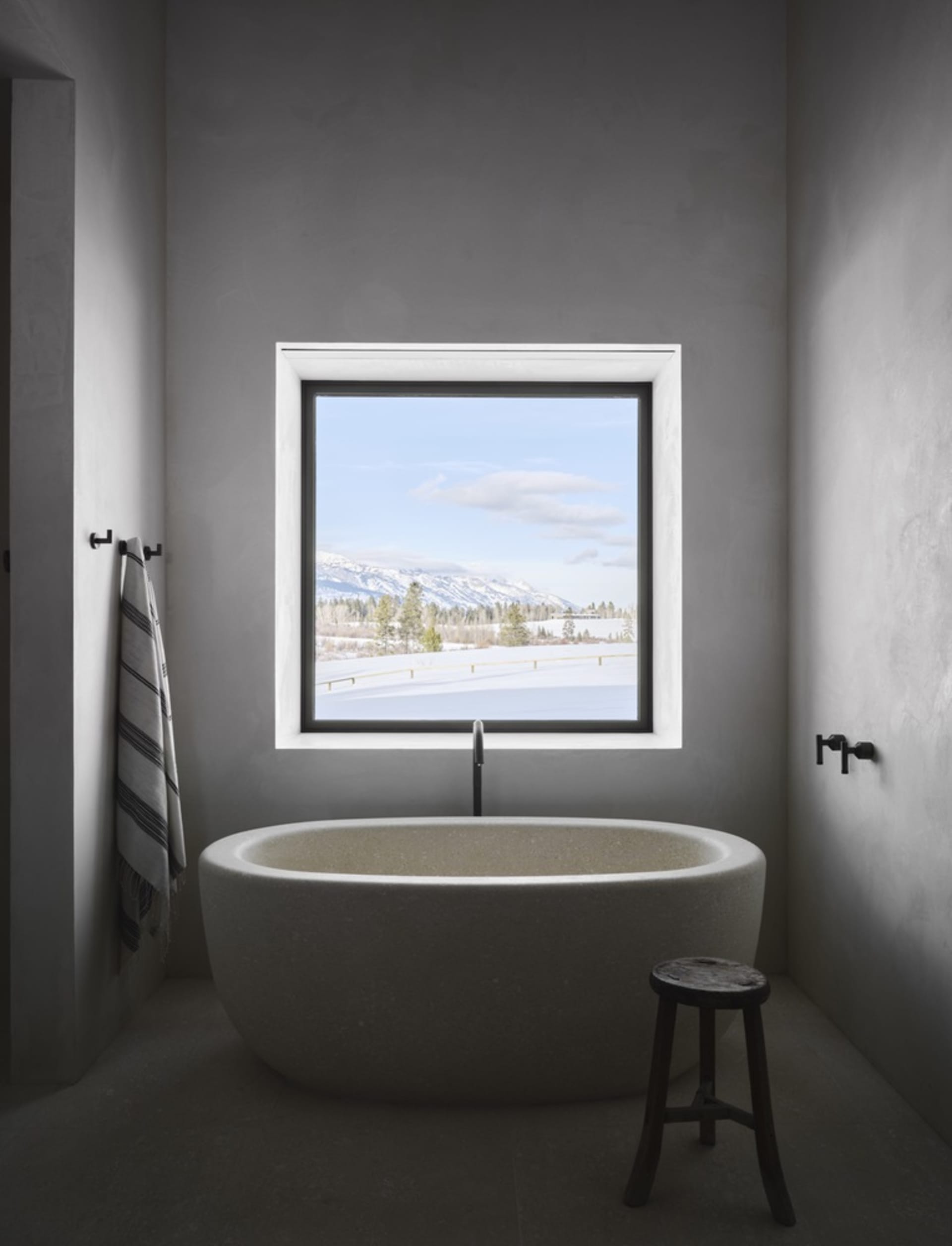 Modern bathroom with a concrete bathtub, designed with a minimalist aesthetic, featuring a window with a scenic view.