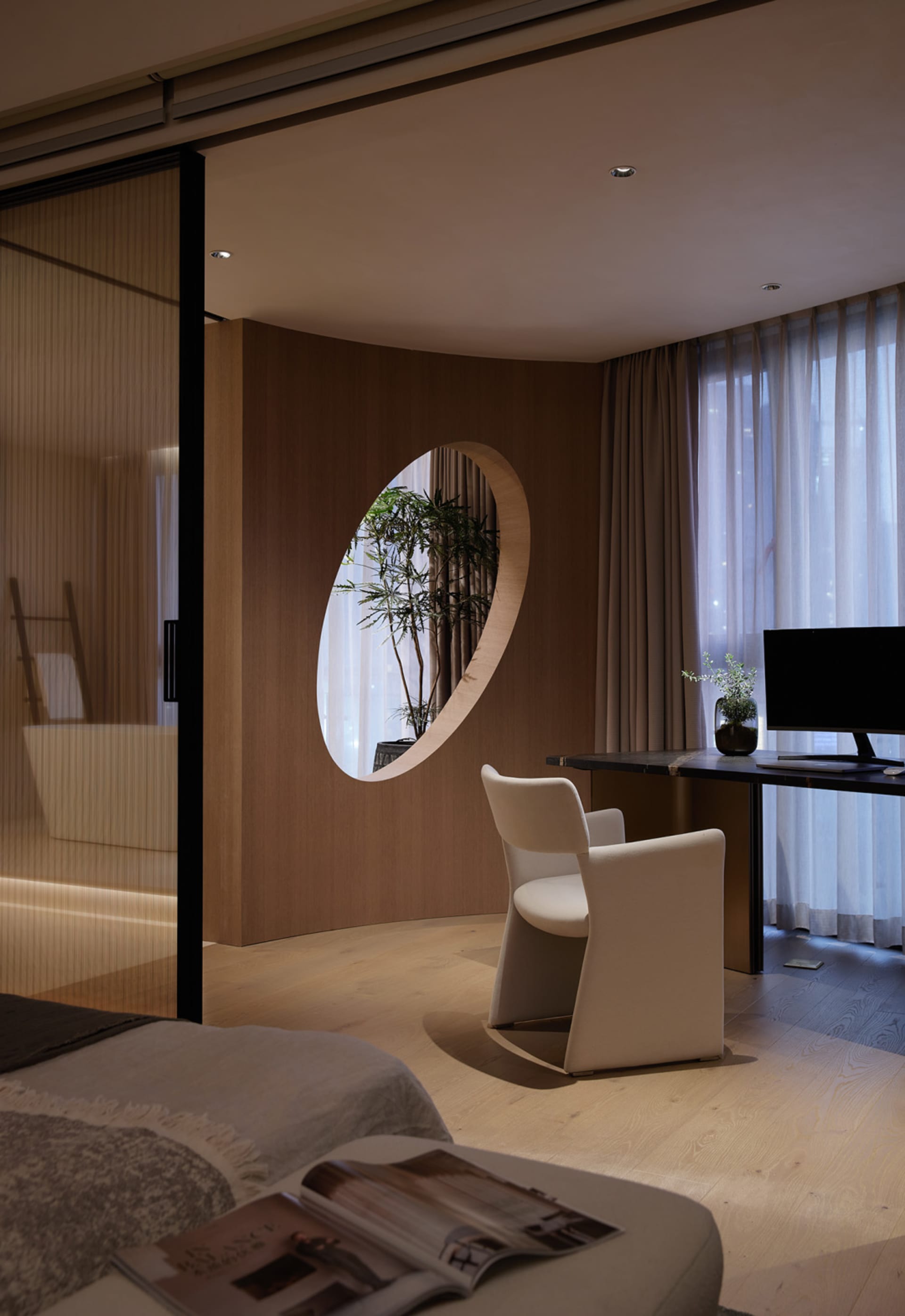A minimalist office space featuring a transparent oval window overlooking greenery.