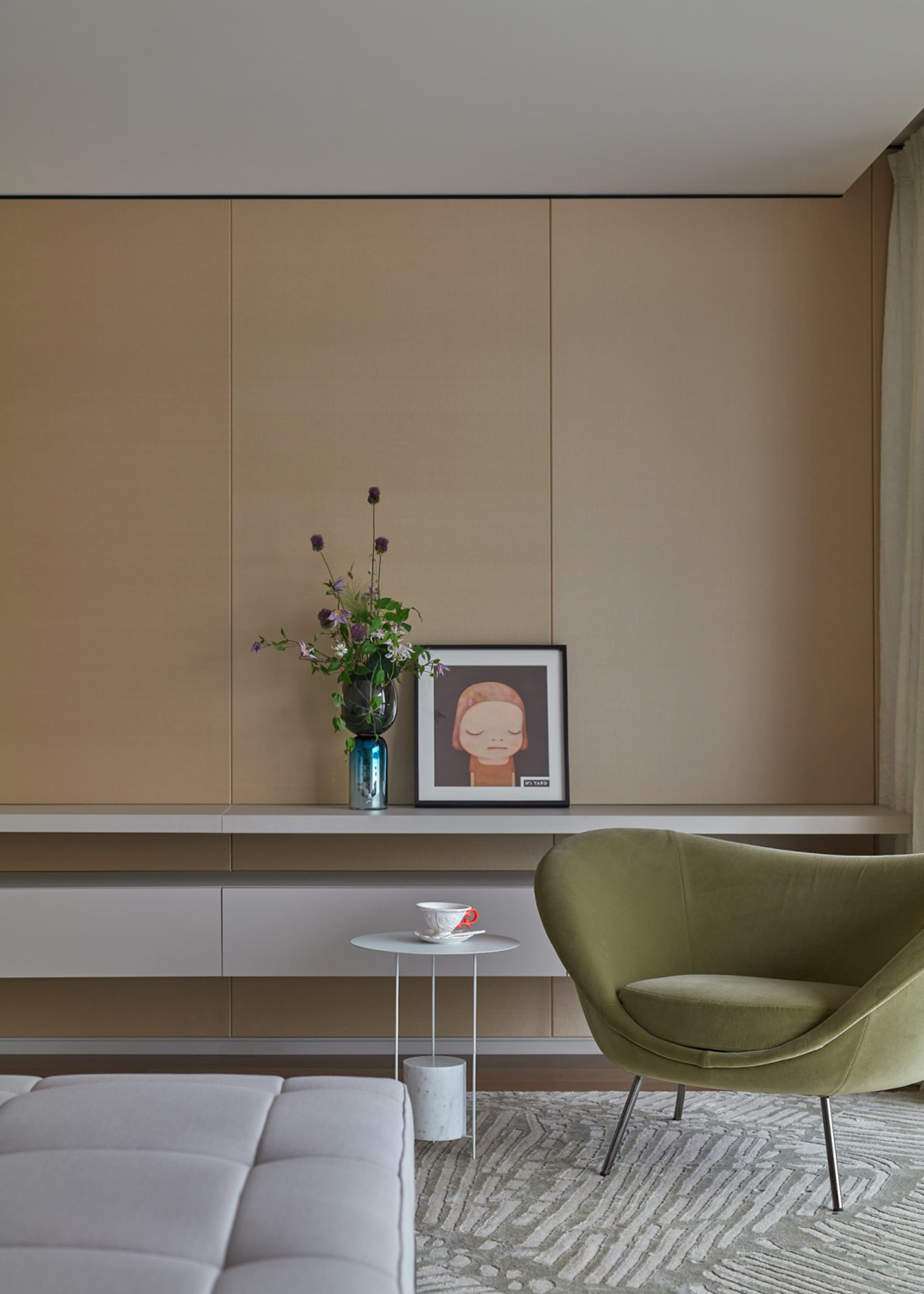 A modern living room with minimalist furniture, a green armchair, and a white sofa against a beige wall.