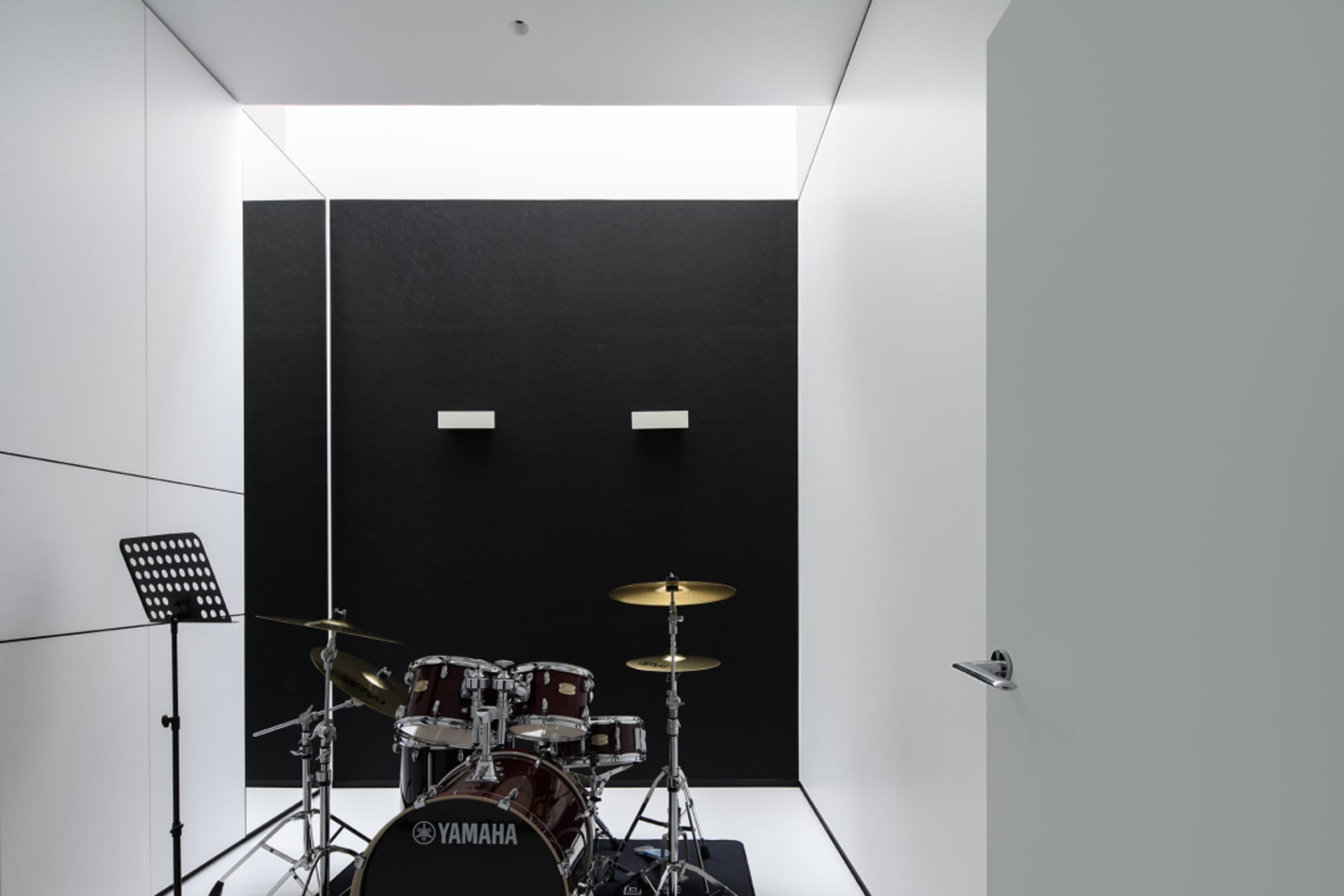 A minimalist music room with a black acoustic foam wall and a Yamaha drum set.