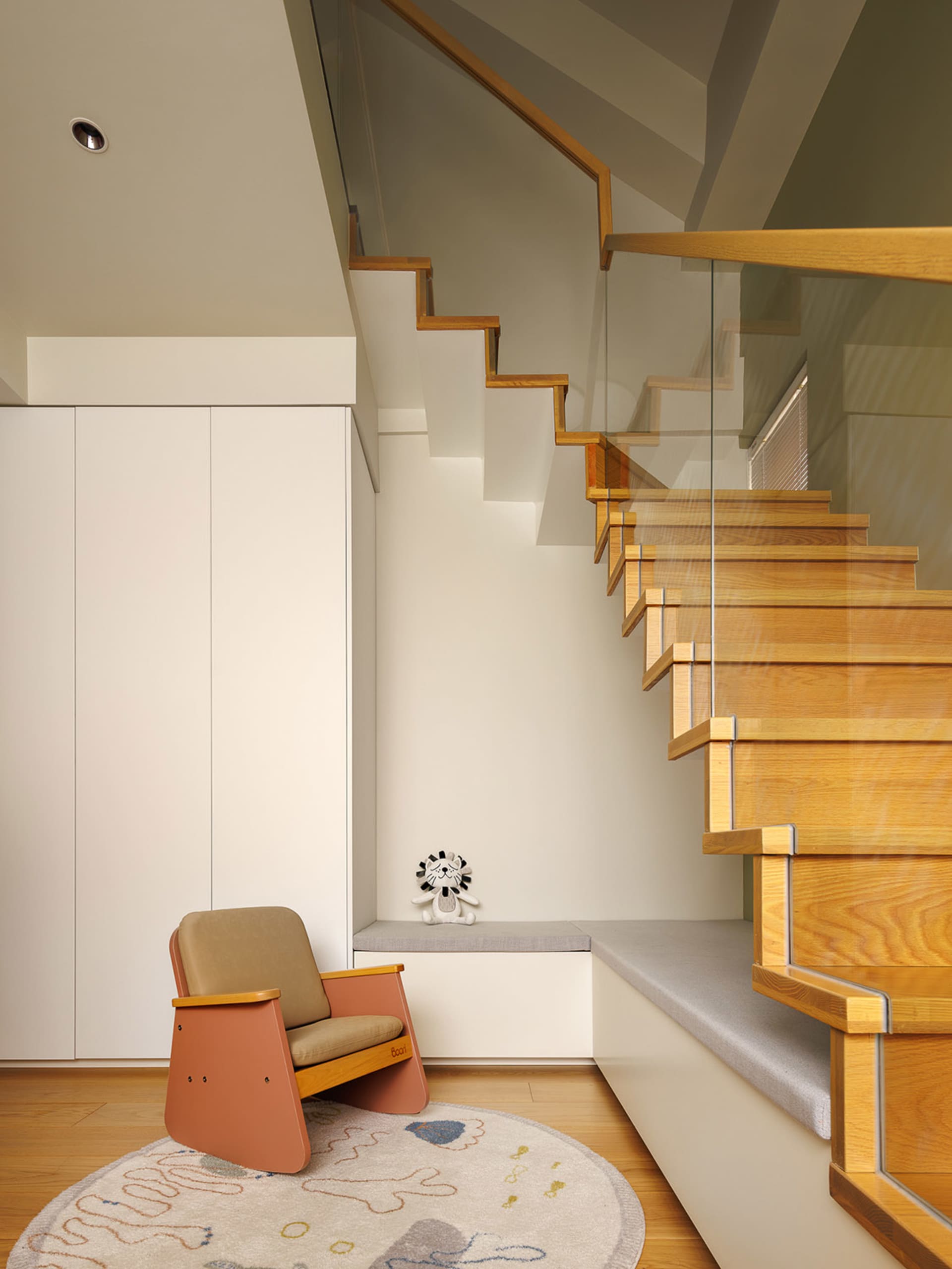 A modern living space featuring a wooden staircase with glass railings and a cushioned bench seat at the landing.