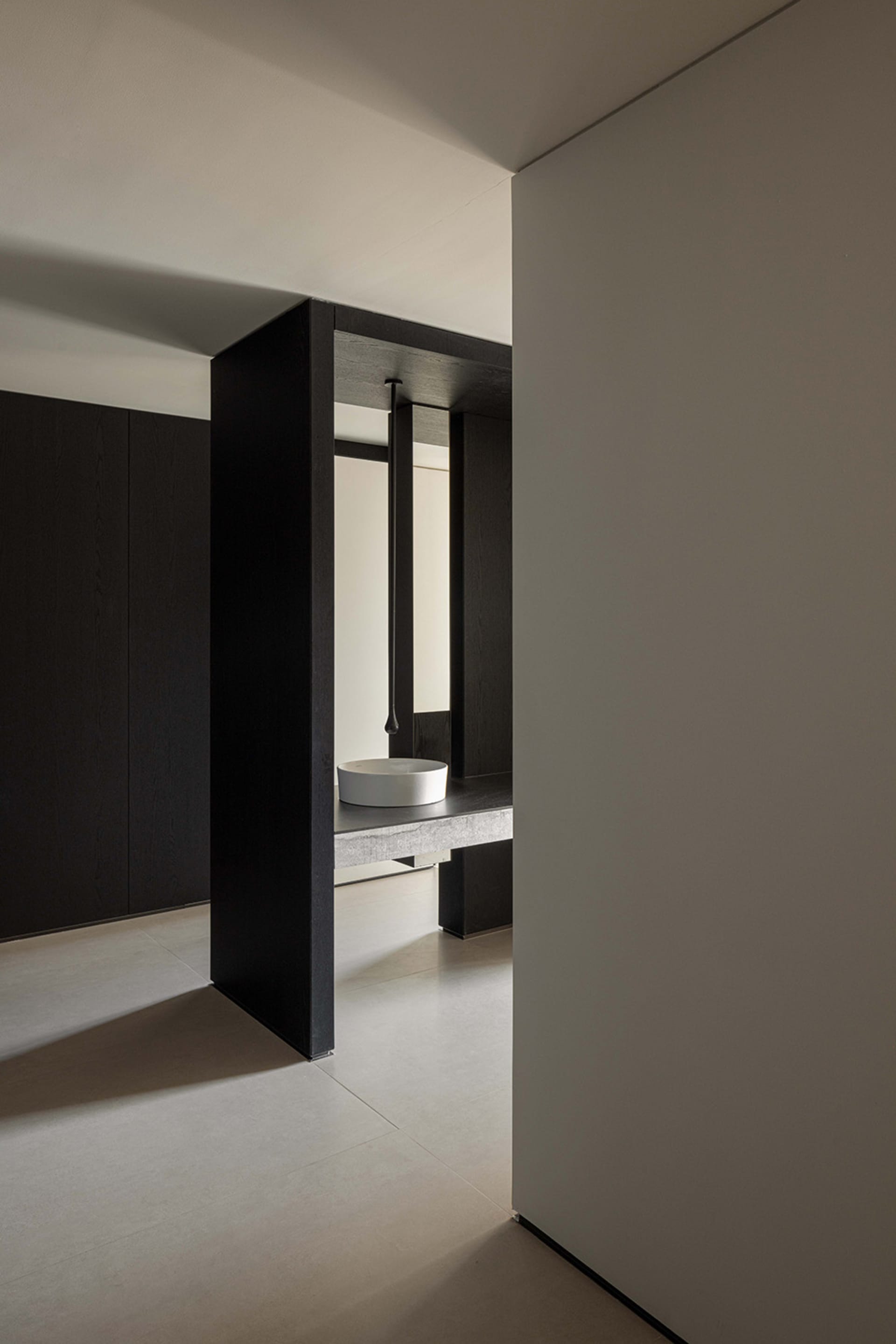 A modern minimalist bathroom with light concrete walls, black wood elements, and sleek lighting design.