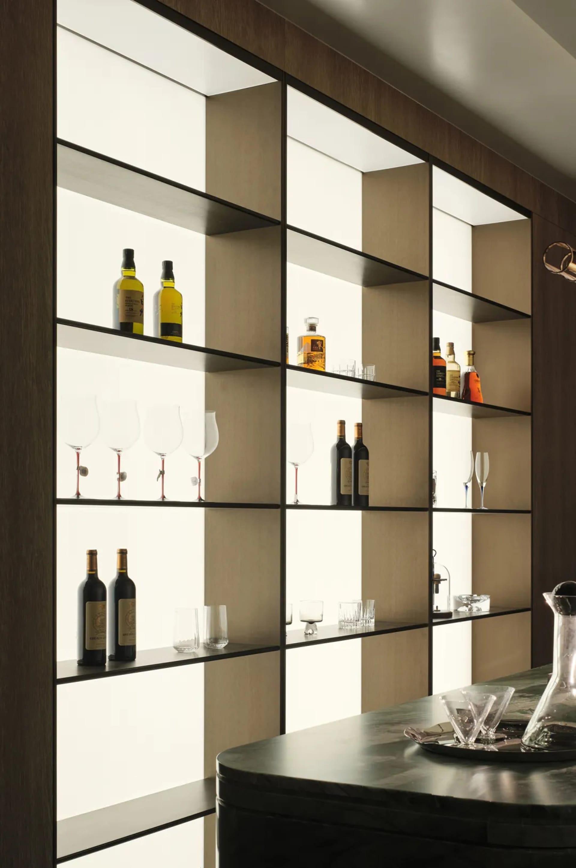 Modern minimalist bar with illuminated glass shelving displaying bottles and glasses.