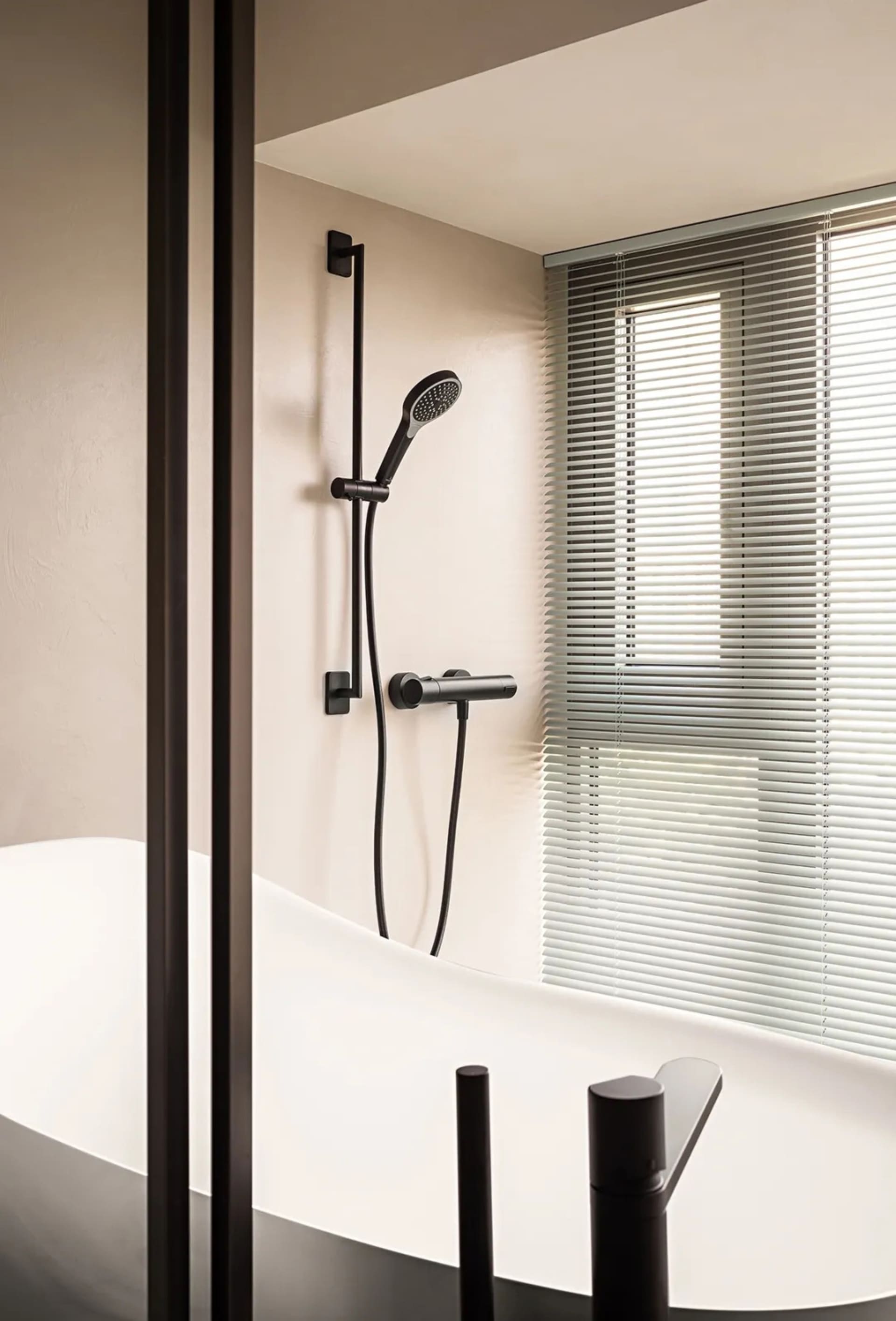 Minimalist bathroom with metallic fixtures and a white bathtub, featuring a shower head and controls.