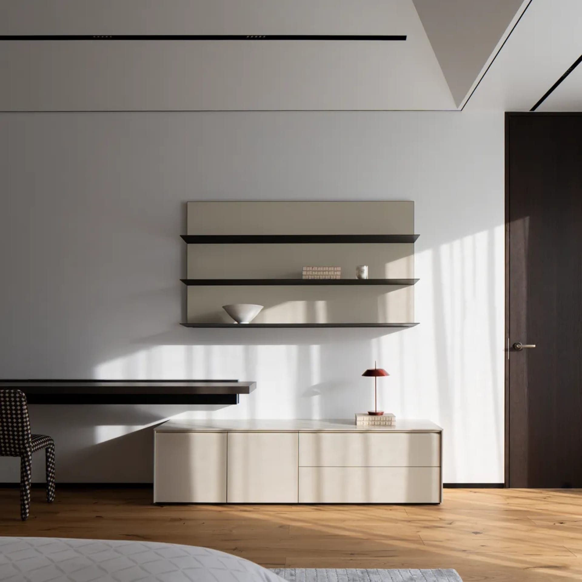 Minimalist bedroom featuring wood flooring and furniture, with a white wall and a floating shelf.