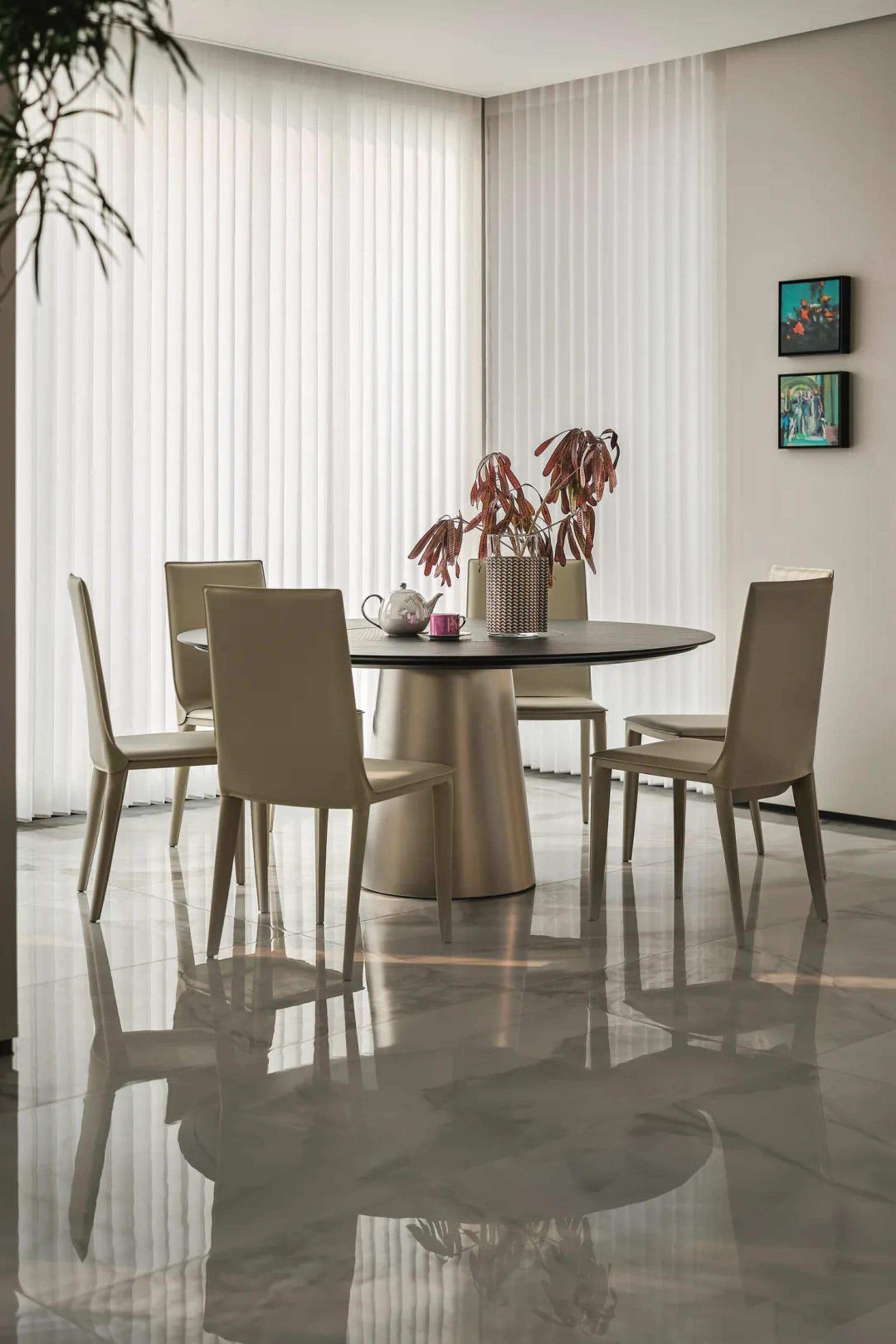 A modern dining room with a round wooden table, white vertical blinds, and white leather chairs.