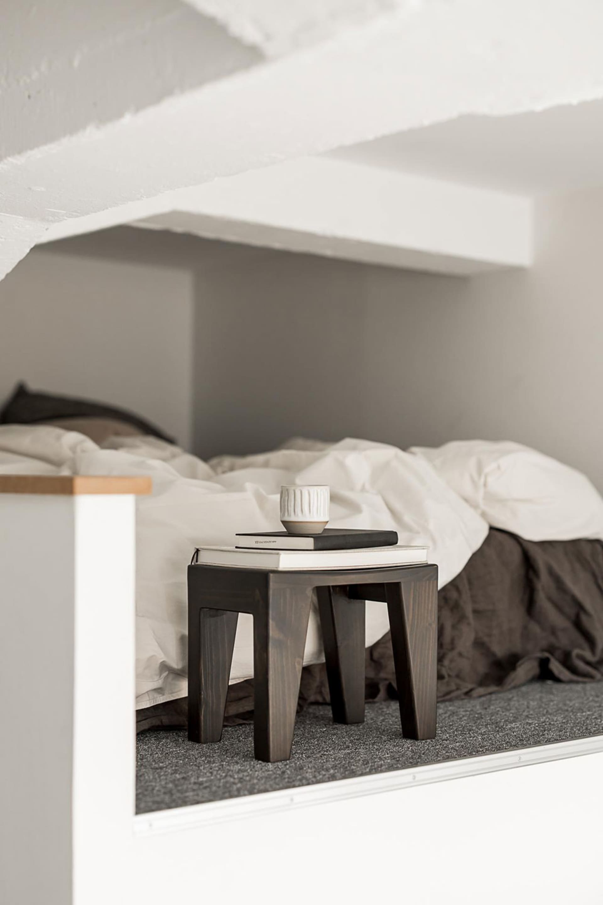 A minimalist bedroom featuring a wooden bedside table with books and a mug on top.