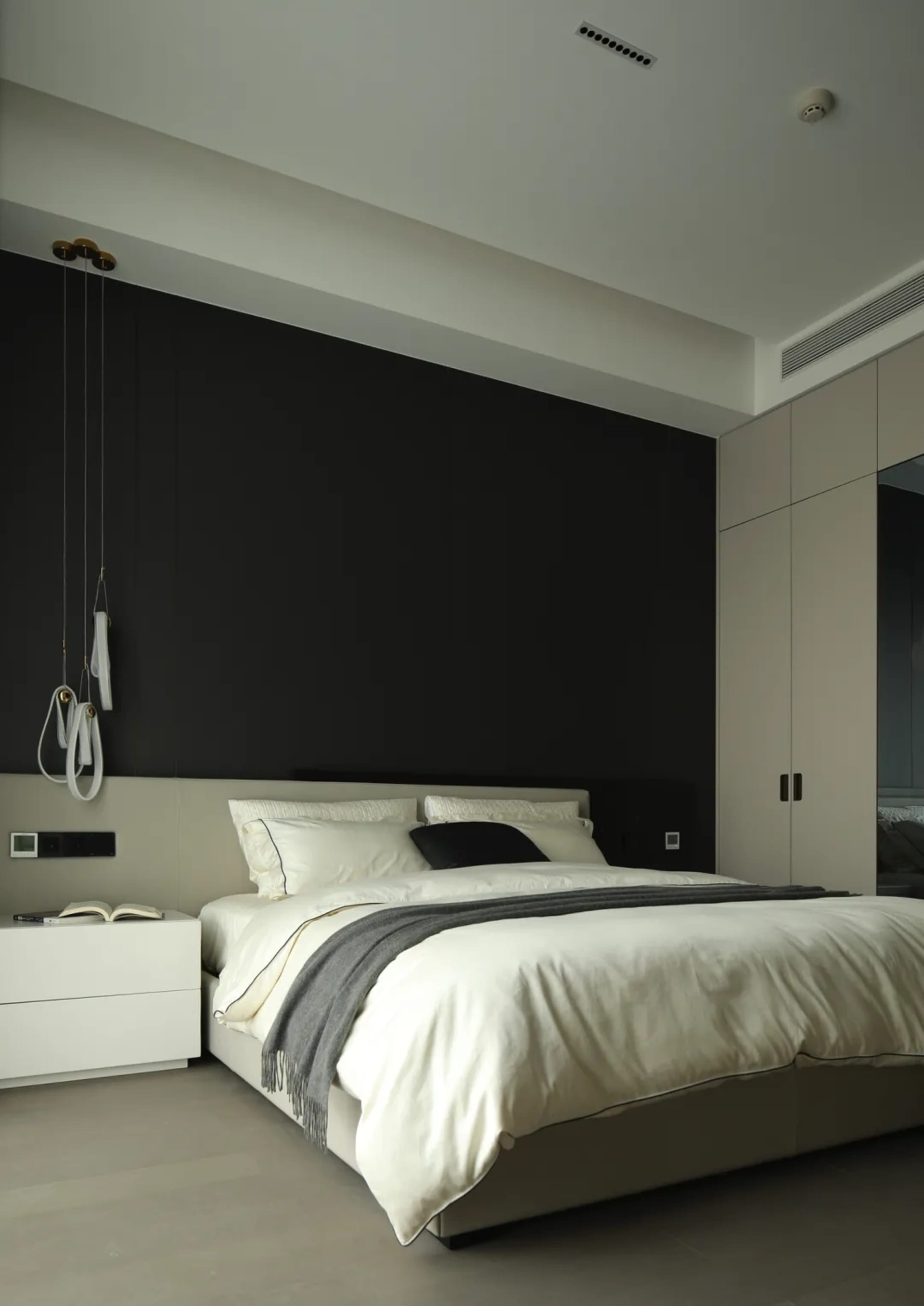 A modern bedroom featuring a black accent wall, white bedding, and minimalist decor.