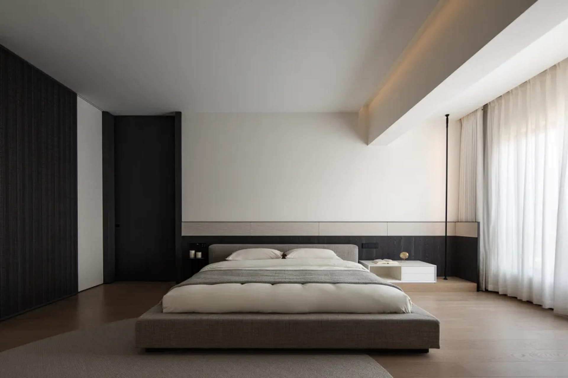 A modern minimalist bedroom with a low-profile bed, light wood flooring, and sleek white walls.