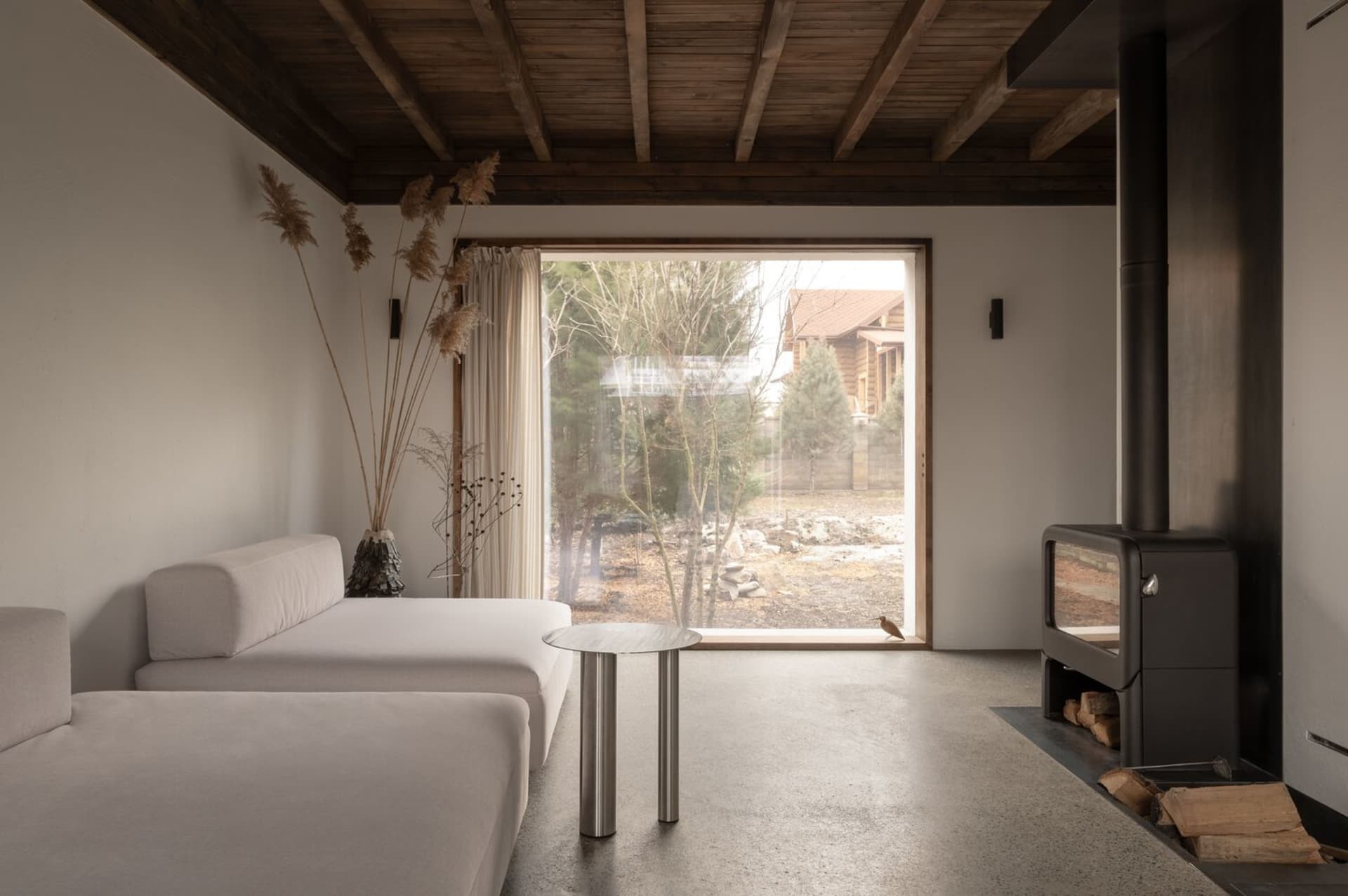 A minimalist living room with concrete elements, including a concrete floor and furniture. Large window provides natural ligh