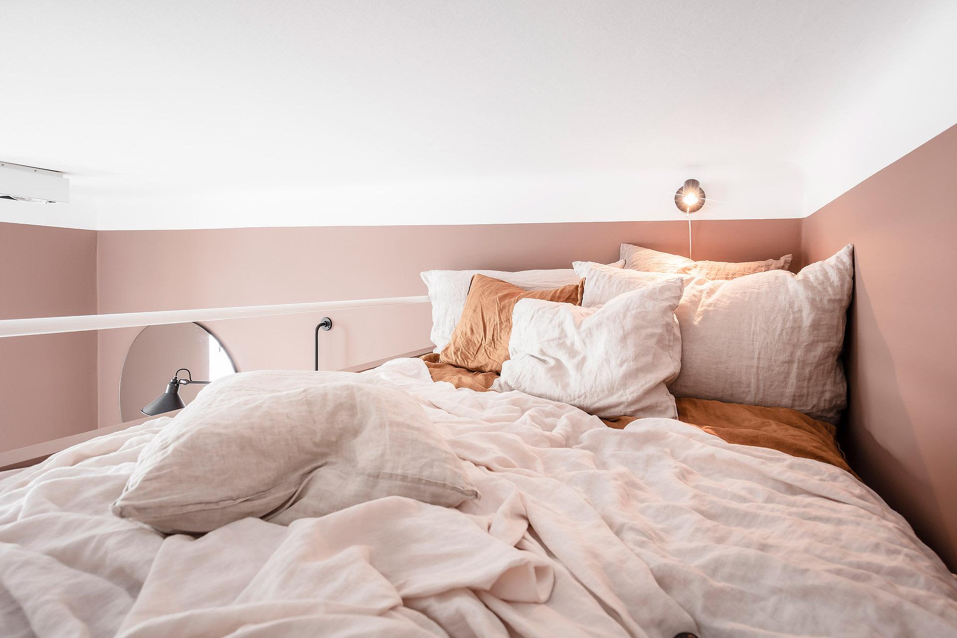 A cozy bedroom featuring a bed covered in a linen-cotton blend comforter and pillows, with a warm-toned wall and ambient ligh