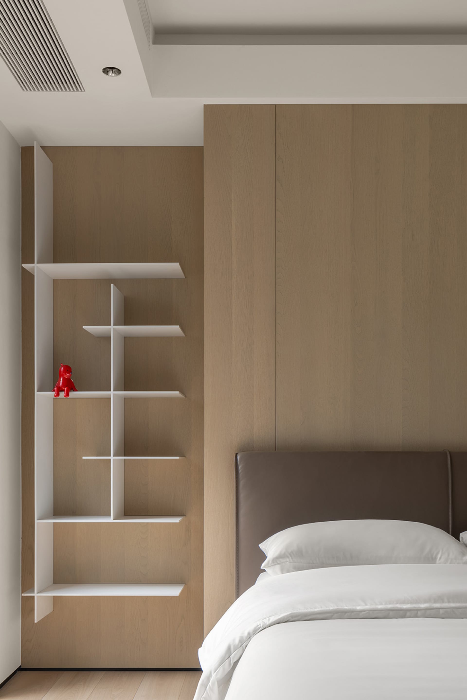 Minimalist bedroom featuring a brown wooden wall panel, a white bed with white pillows, and a white shelf system.