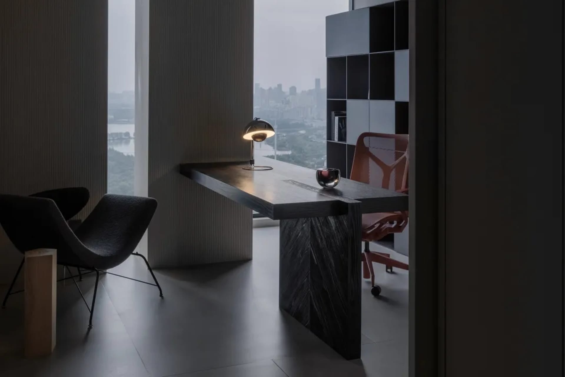 Modern office space featuring minimalist design with wooden desk and metal chair, and a view of the city through the large wi