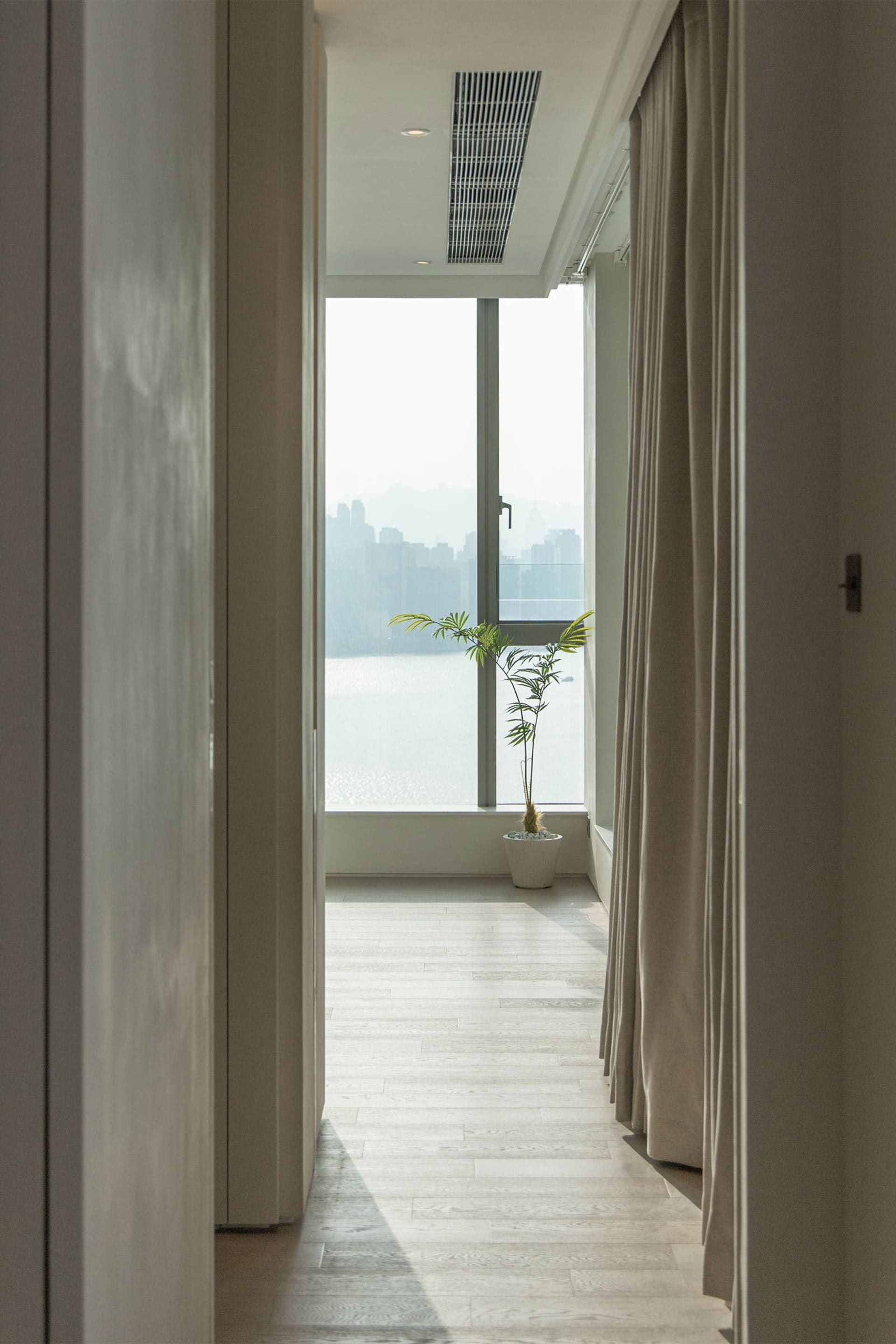 A modern residential hallway featuring white oak wood flooring and a view through the window to the cityscape.