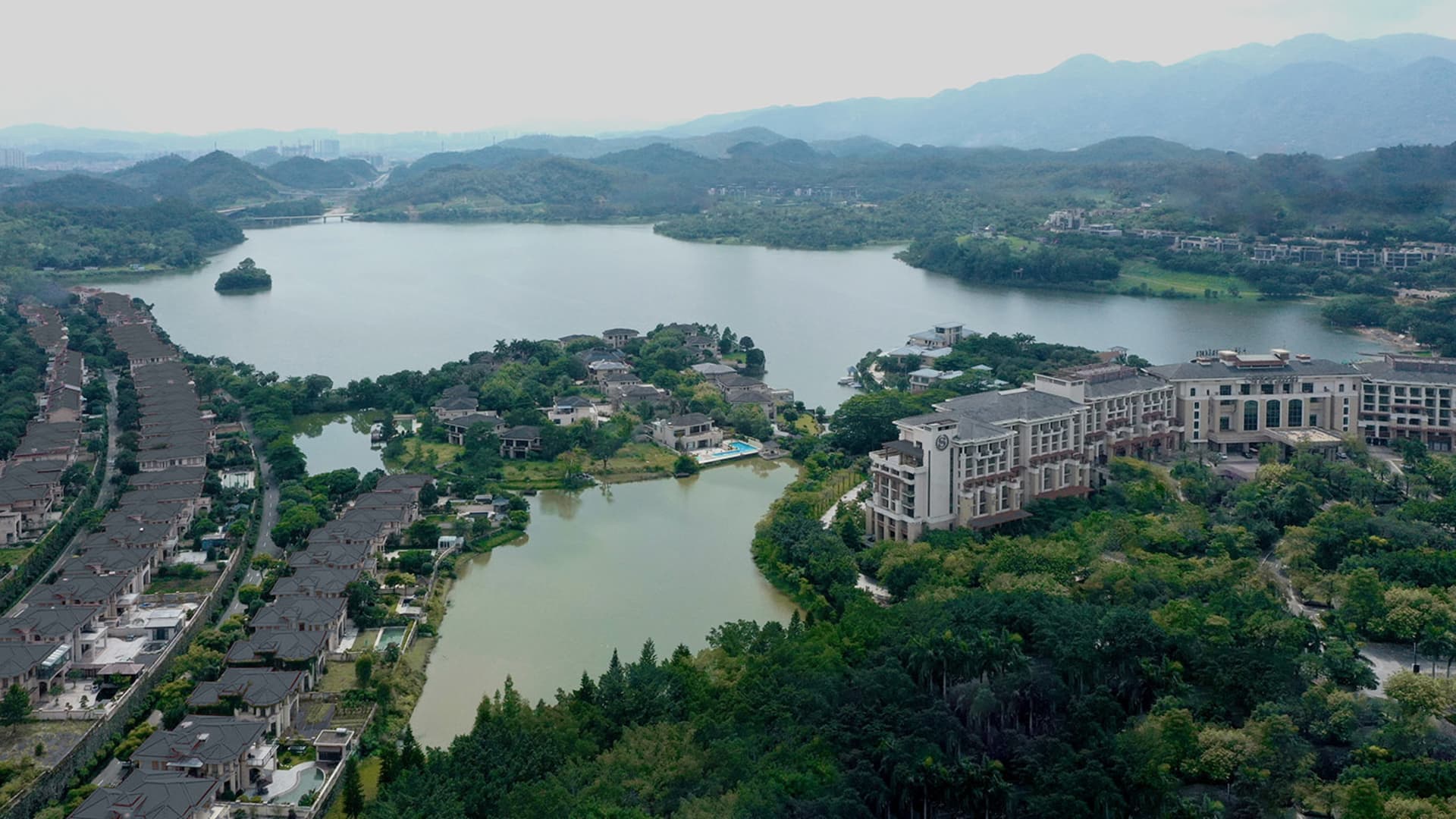 Aerial view of modern residential buildings surrounded by a large lake and greenery.