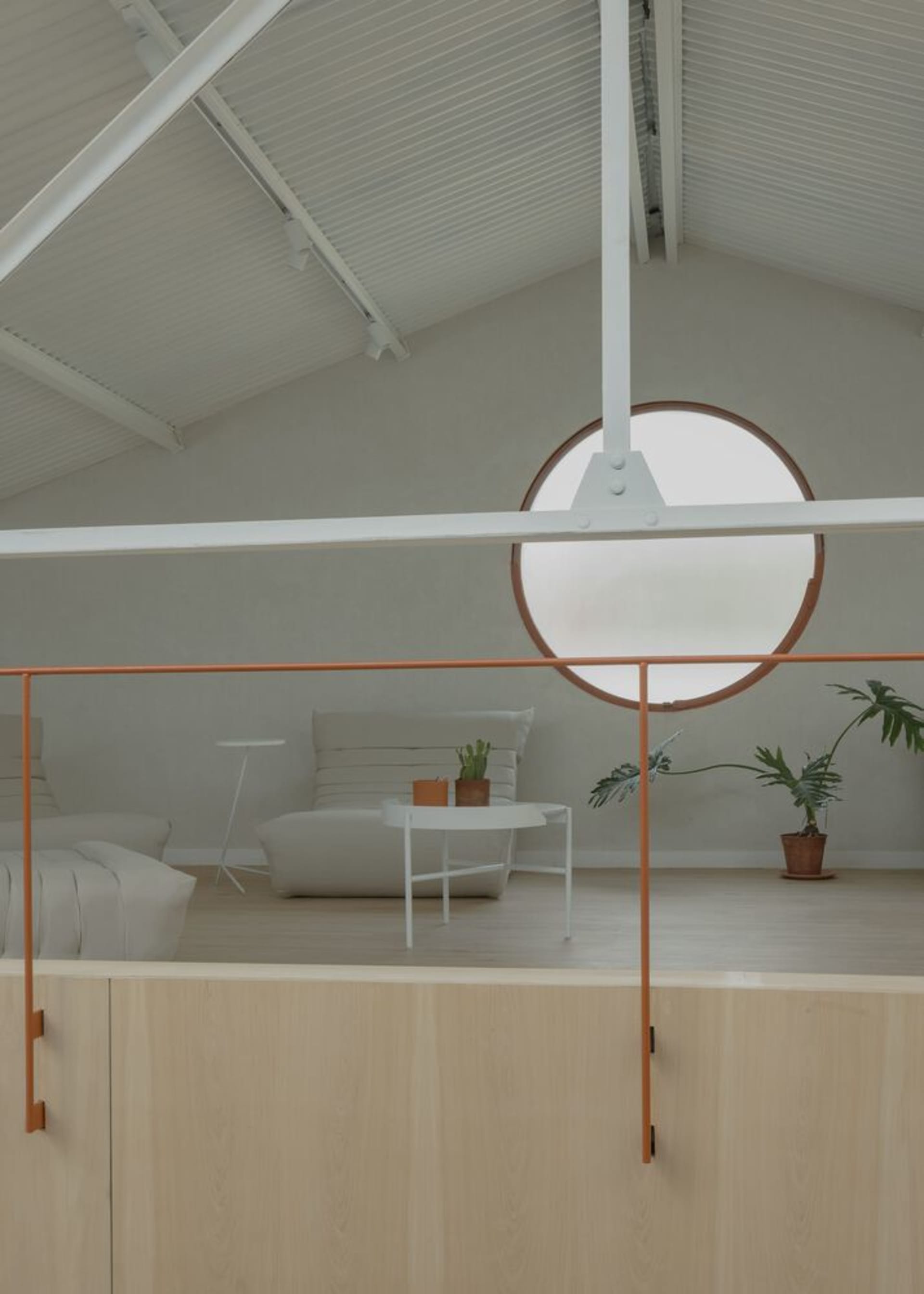 A minimalist living space featuring wood flooring, white furniture, and a circular window.