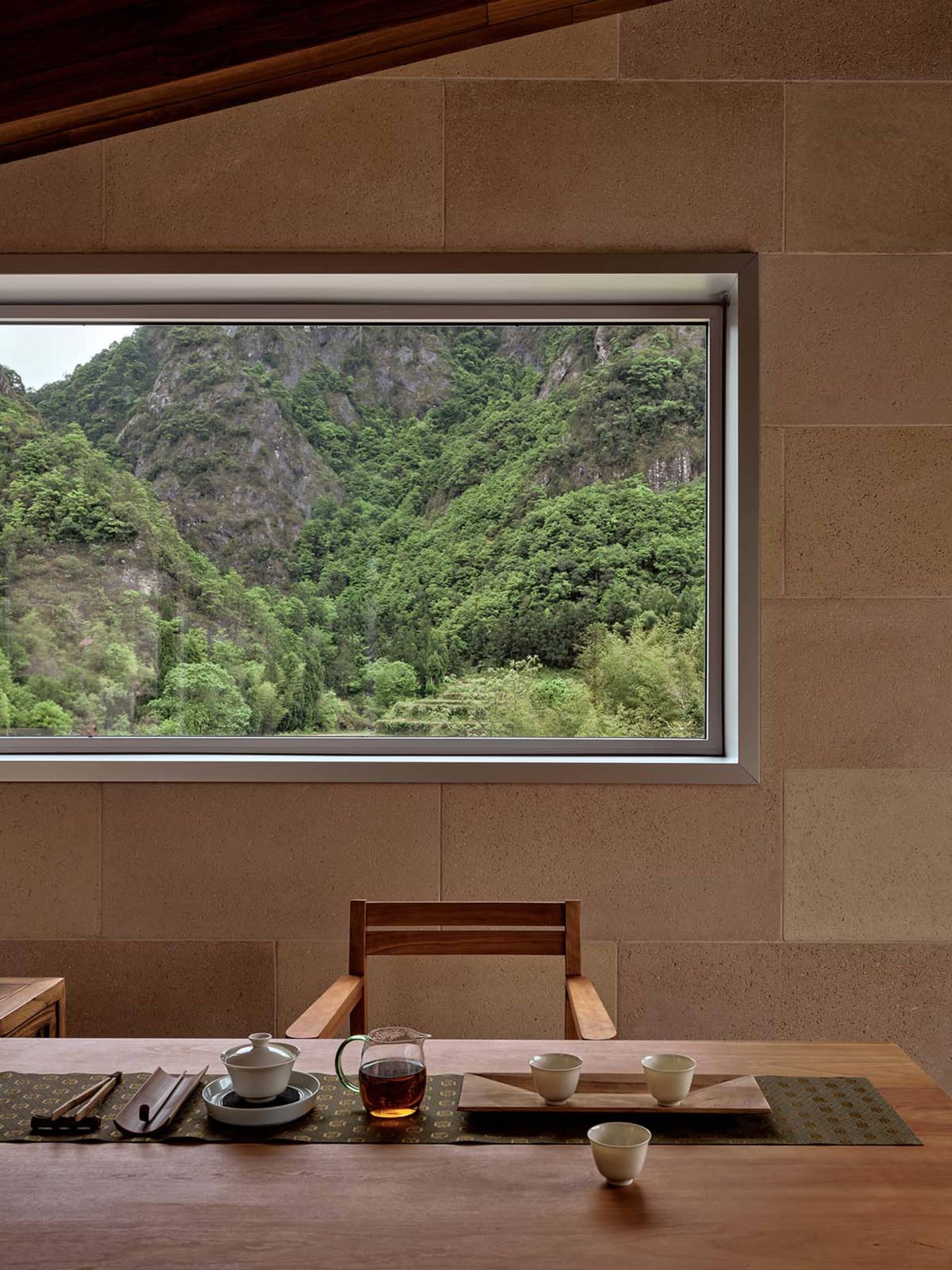 A minimalist tea room featuring a wooden table set with traditional tea utensils, surrounded by a natural stone wall and fram