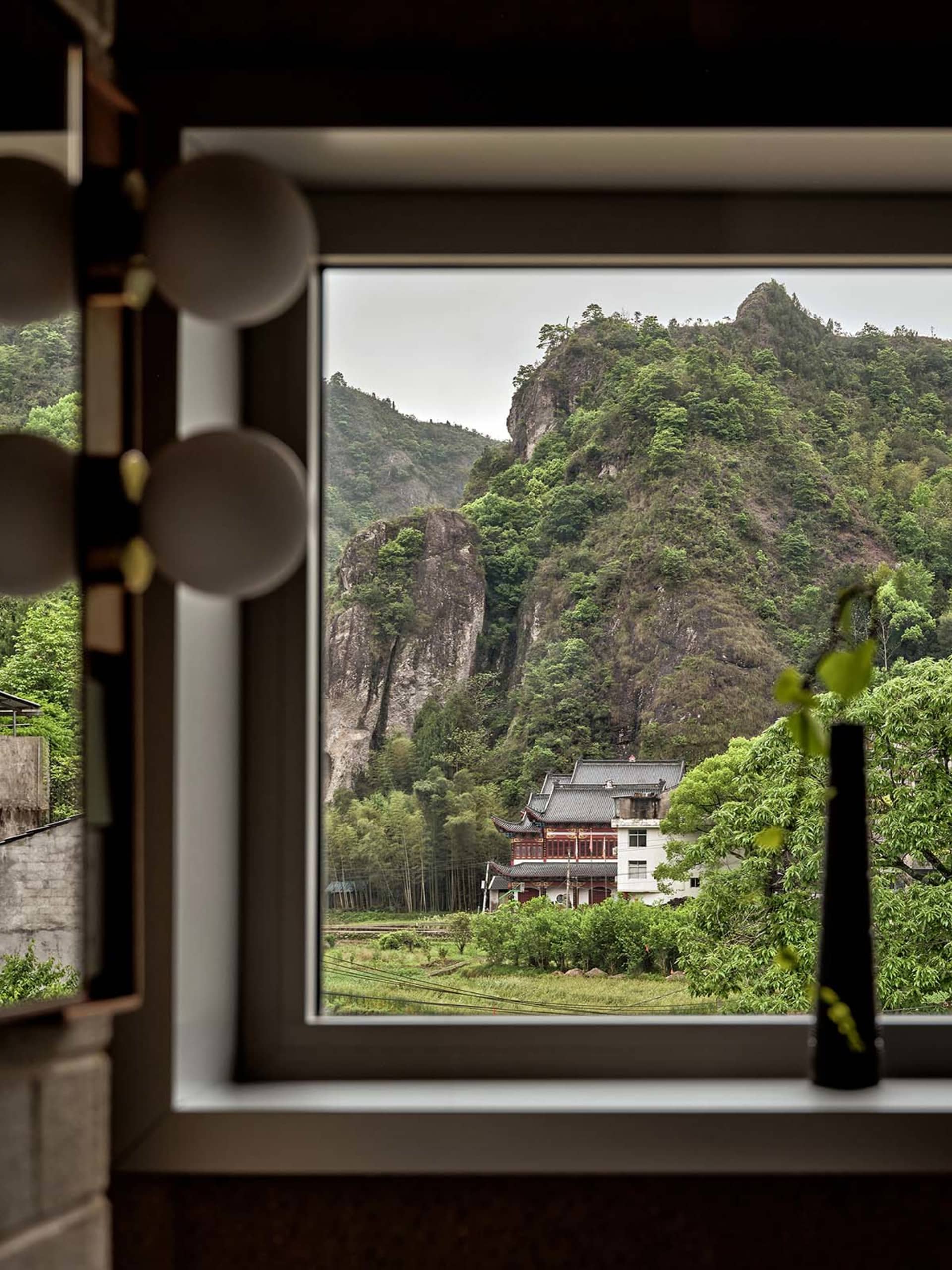 窗戶外眺望茂密山景，傳統建築隱藏於樹叢之中。