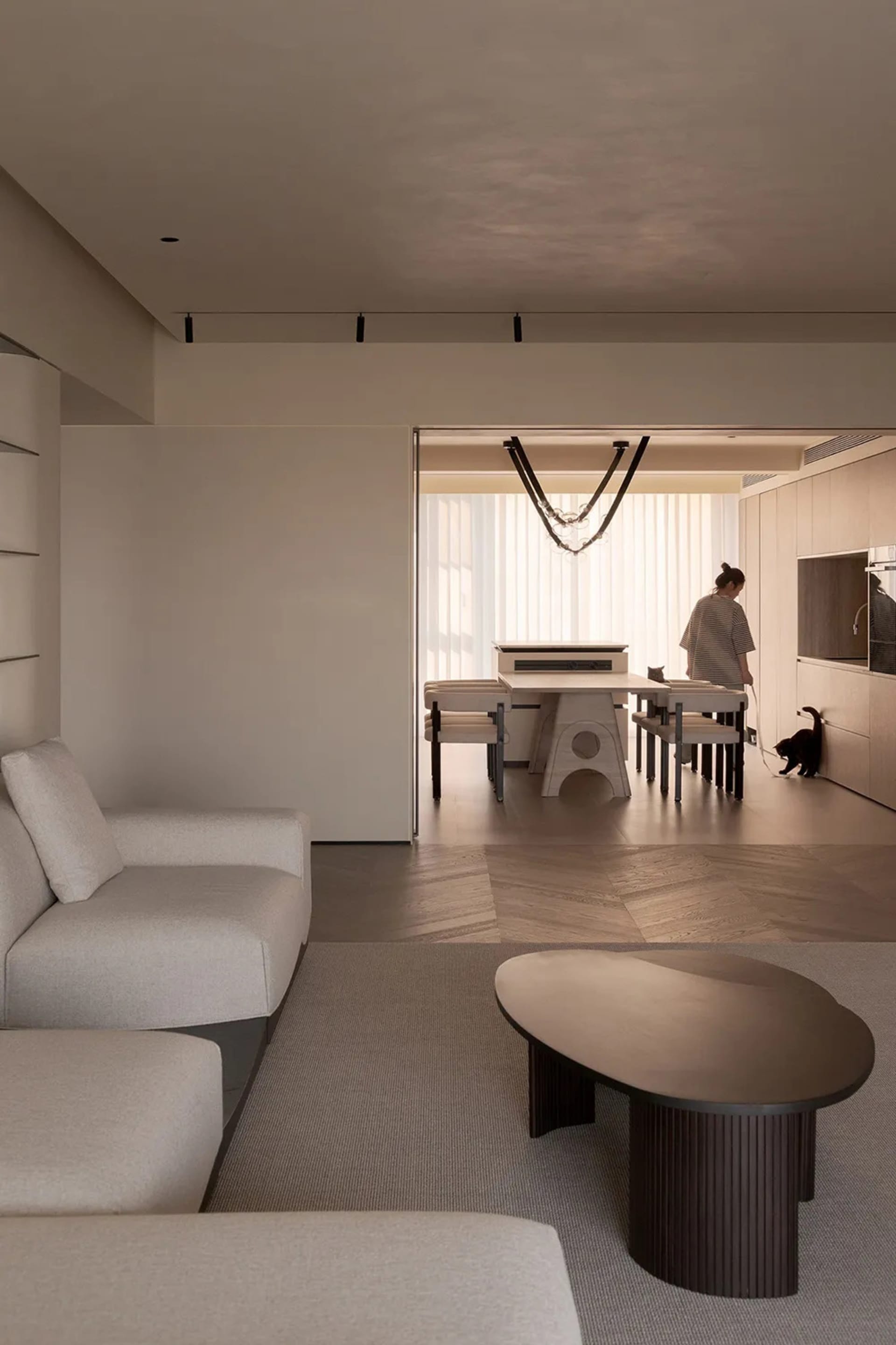 Modern minimalist living room with neutral tones, featuring a large sofa, a round coffee table, and a dining area in the back
