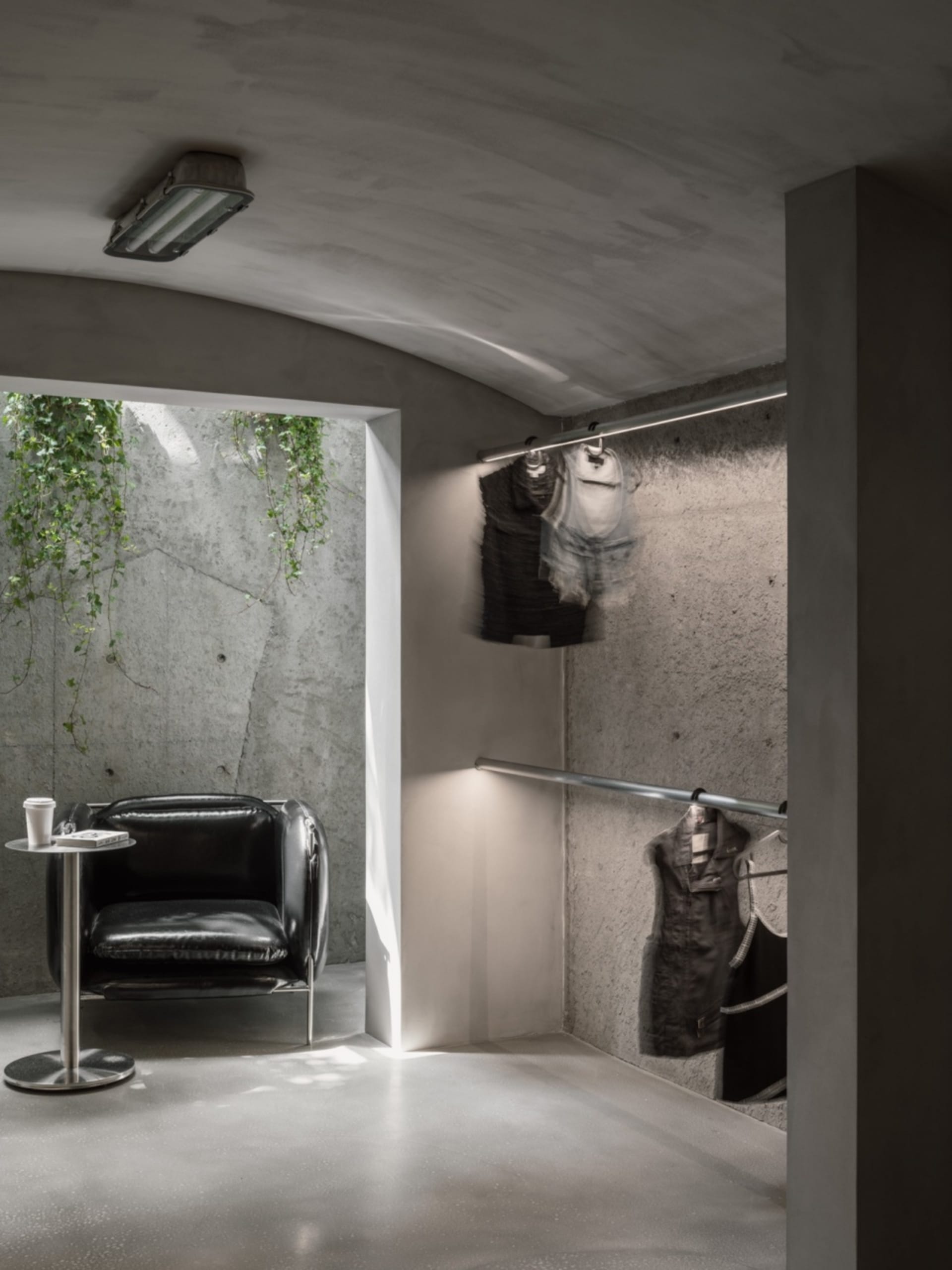 Modern clothing shop with concrete walls, industrial lighting, and minimalist black armchair.