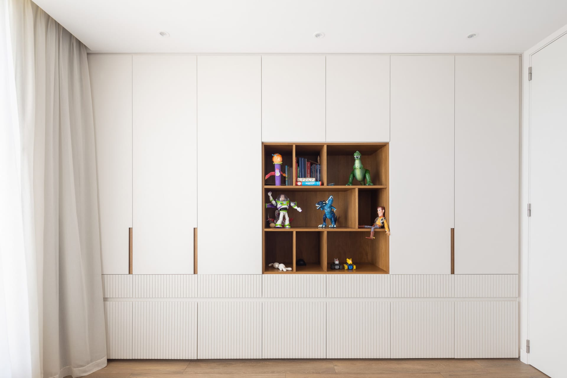 A modern white children's playroom with shelves displaying toys and books.