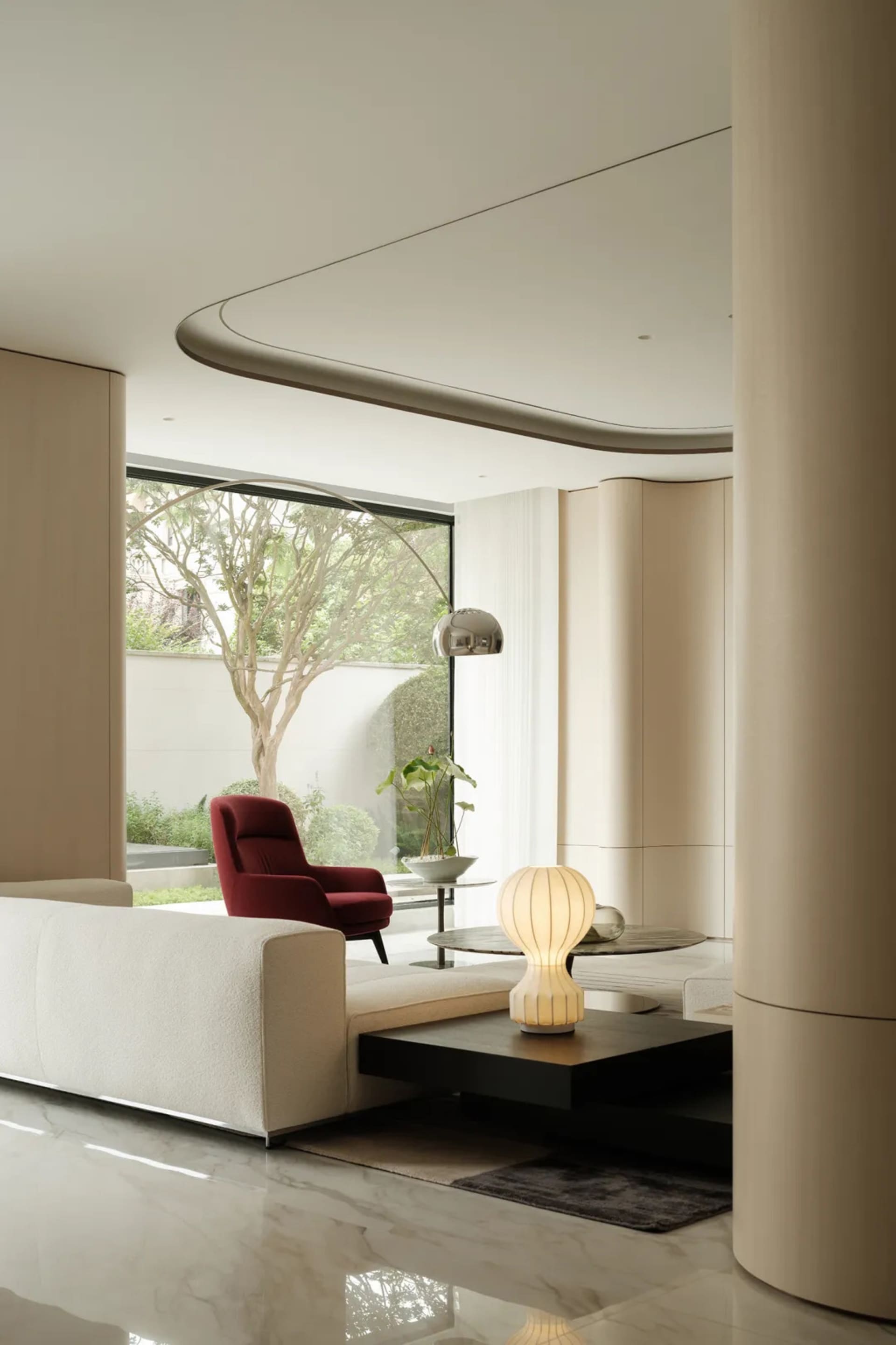 A minimalist modern living room with white furniture, a red armchair, and a glass coffee table.