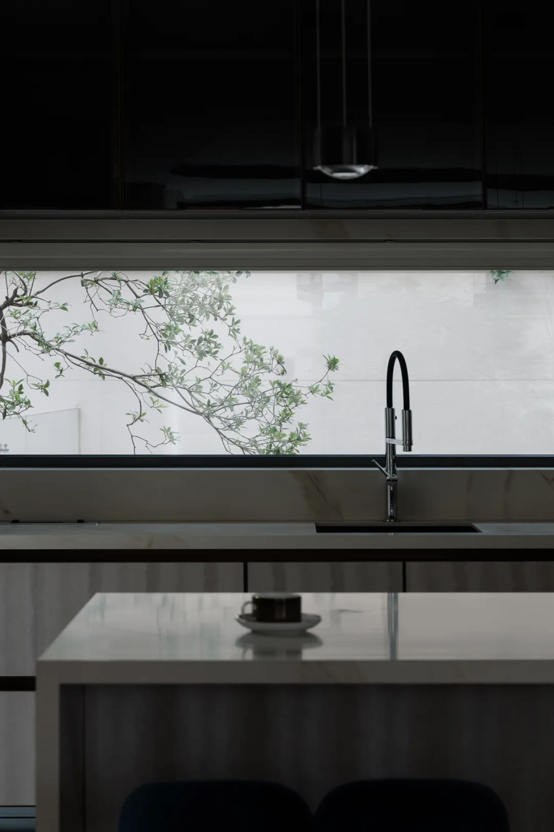 A modern, minimalist kitchen with a marble countertop and a view of greenery outside the window.
