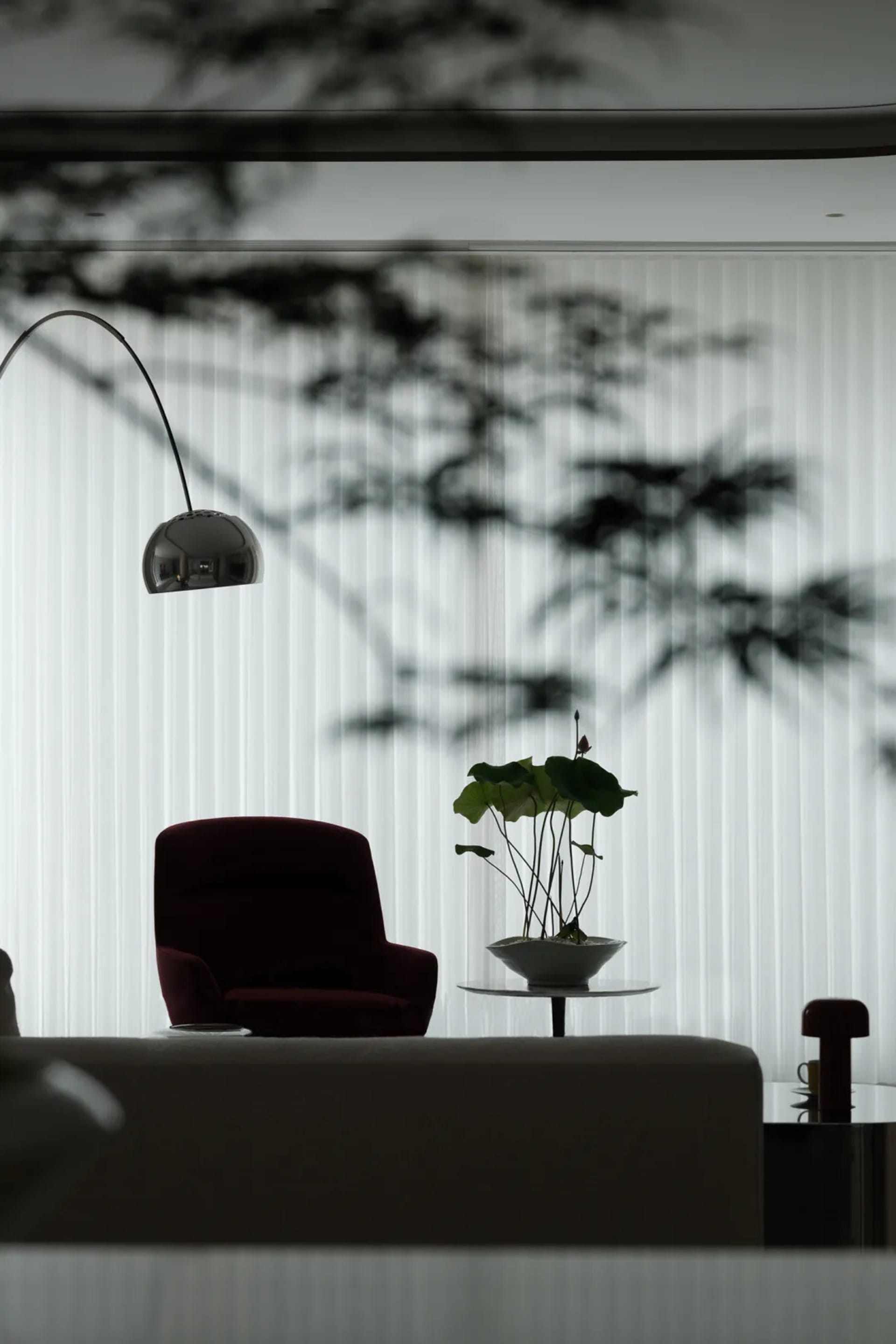 A modern minimalist living room with a glass window, velvet armchair, and potted plant on a side table.