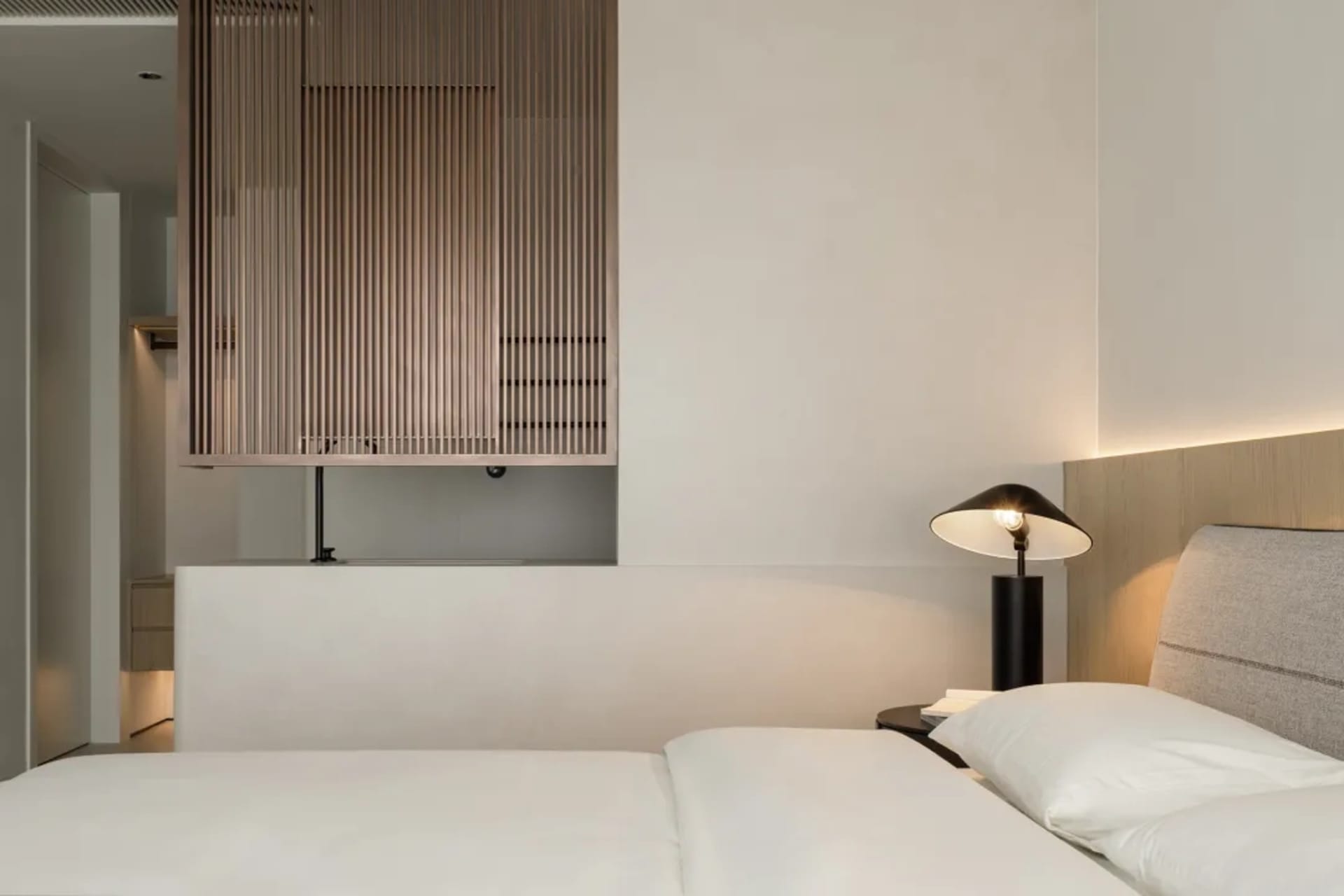 A minimalist bedroom with a white bed, wooden paneling, and modern lamp.