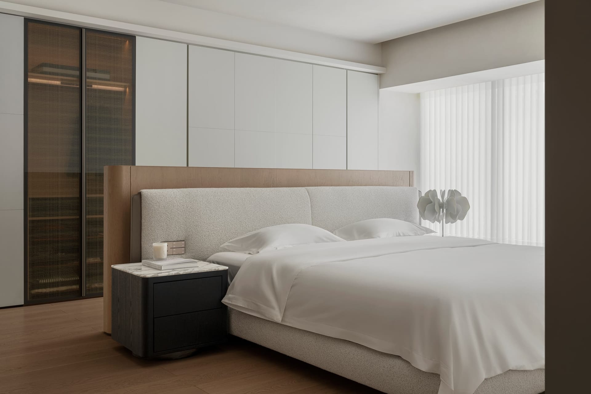 A modern minimalist bedroom featuring a white upholstered bed with a wooden headboard and a minimalistic decorative lamp on a