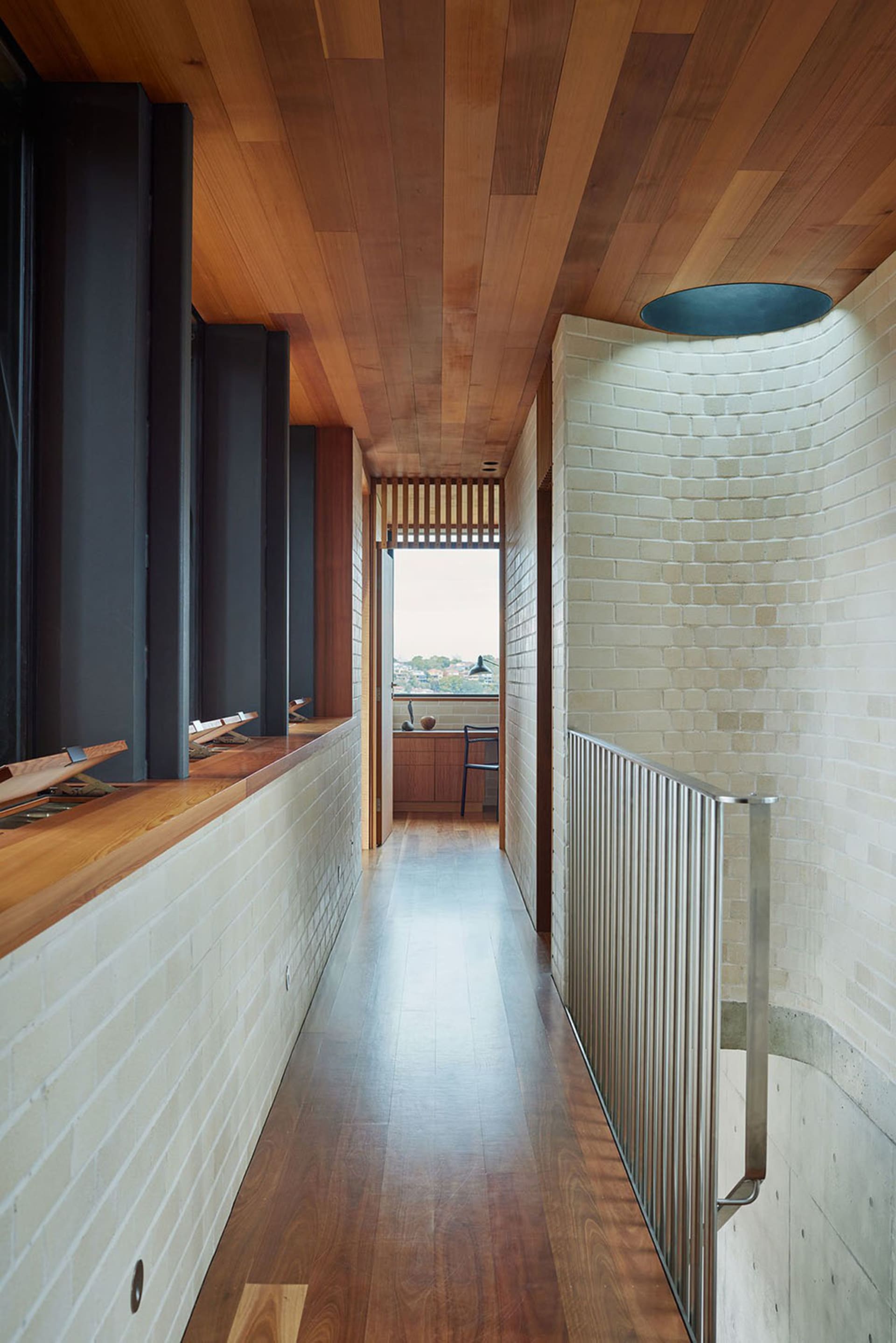 A modern interior featuring wooden ceiling, brick pillar, and metal railing.