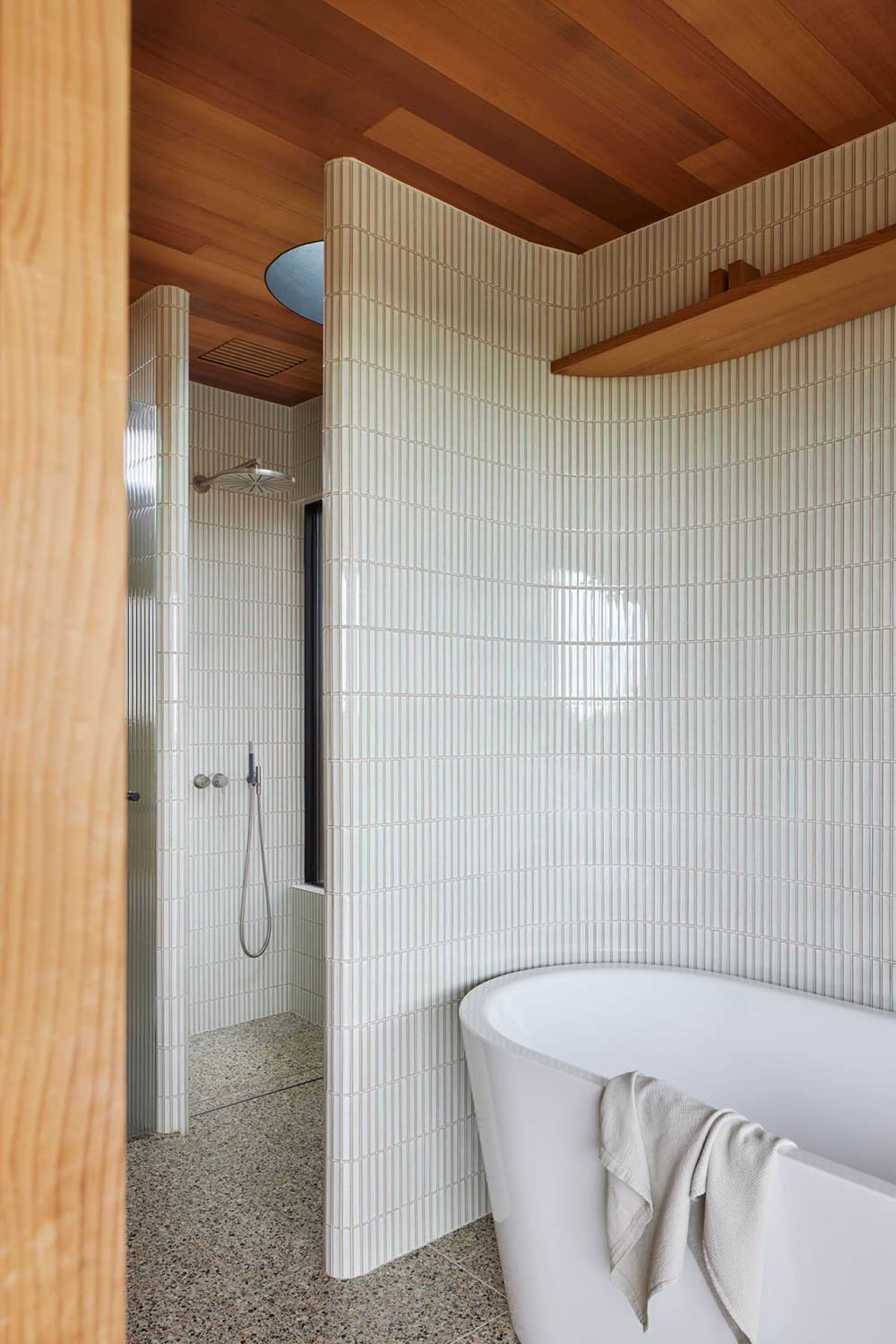 A modern bathroom featuring a freestanding bathtub, tiled shower, and a wooden ceiling with a concrete floor.