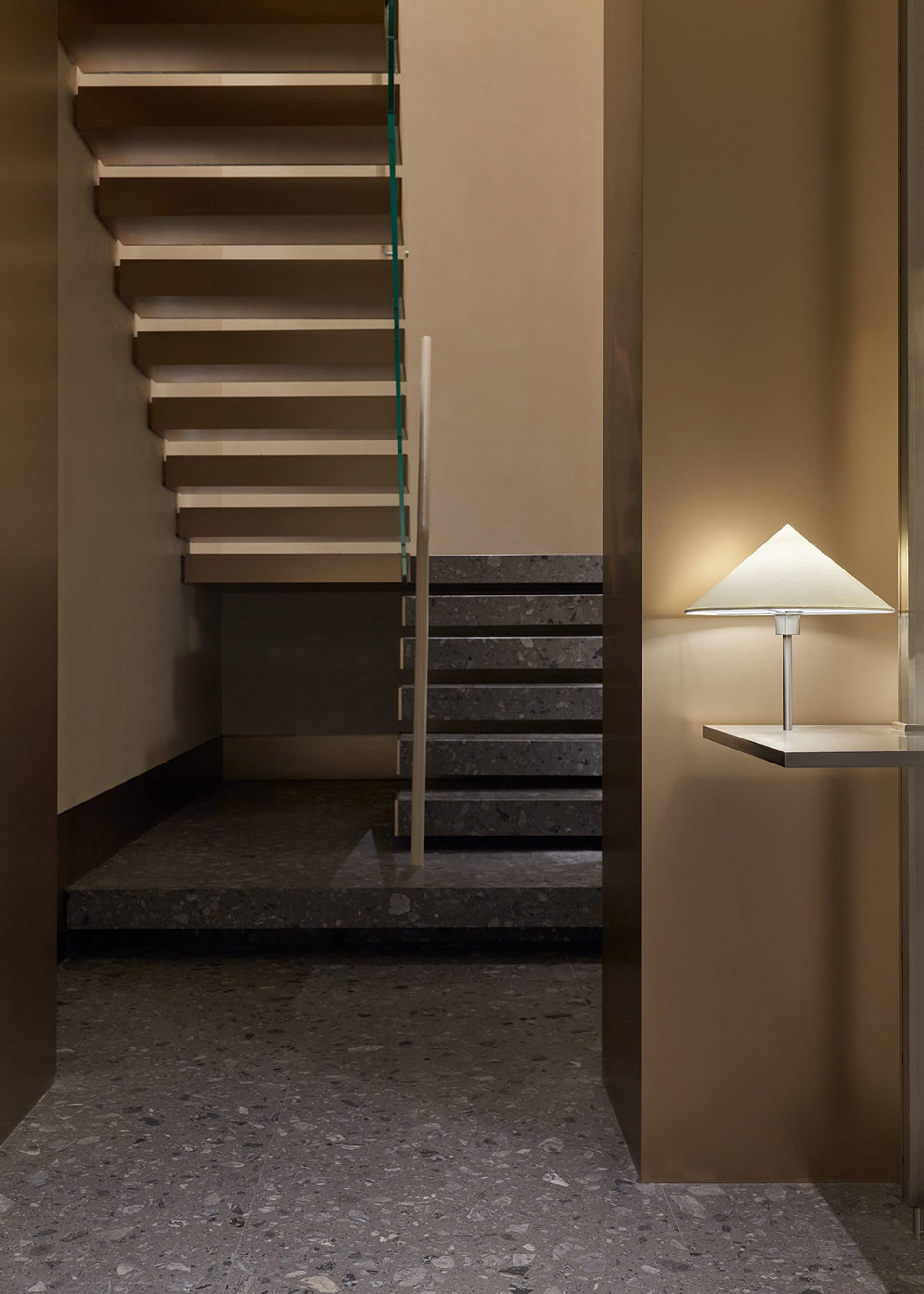 A modern staircase features concrete steps illuminated by a sleek, angular lamp with a triangular shade.