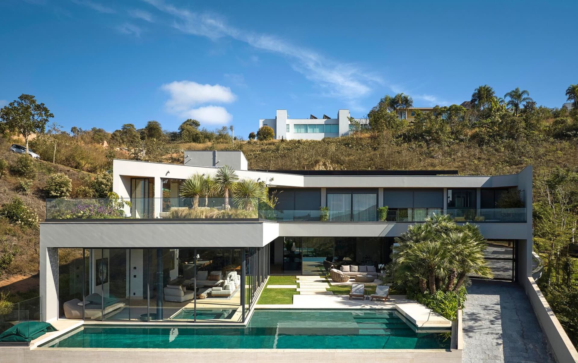 Modern residential house with glass walls, steel accents, and concrete finishing, featuring a swimming pool and lush landscap